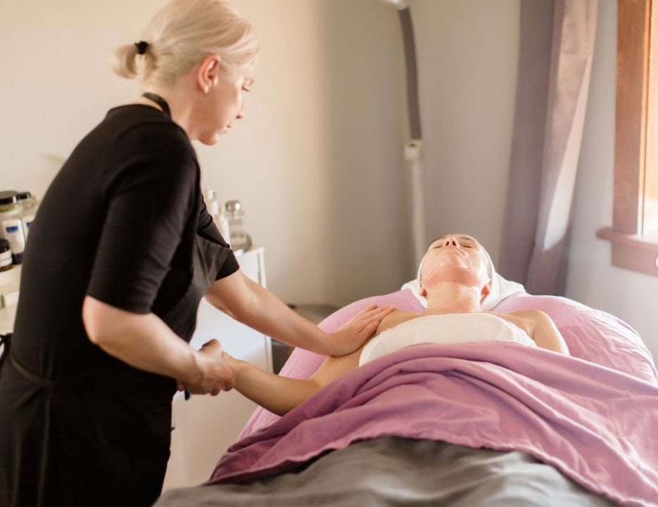 A woman receiving a massage from a massage therapist in a cozy room with natural light.