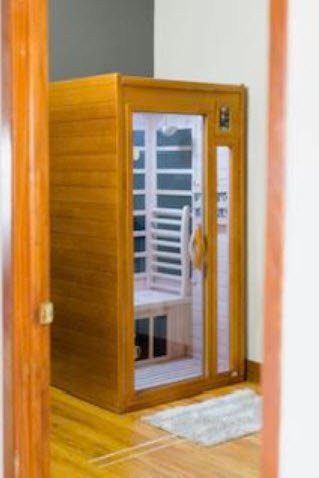 Indoor sauna with wooden exterior and glass door, located in home with hardwood floors and a white rug in front.