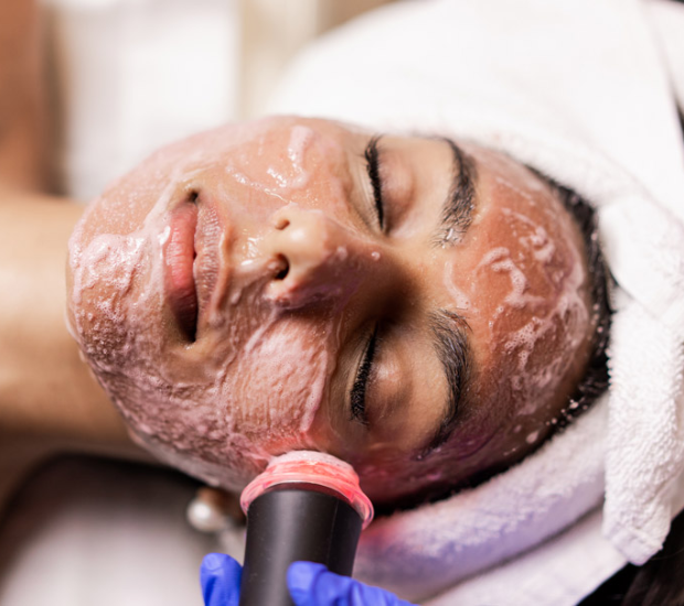 Close-up of a woman receiving a facial treatment with a black device emitting light on her face.