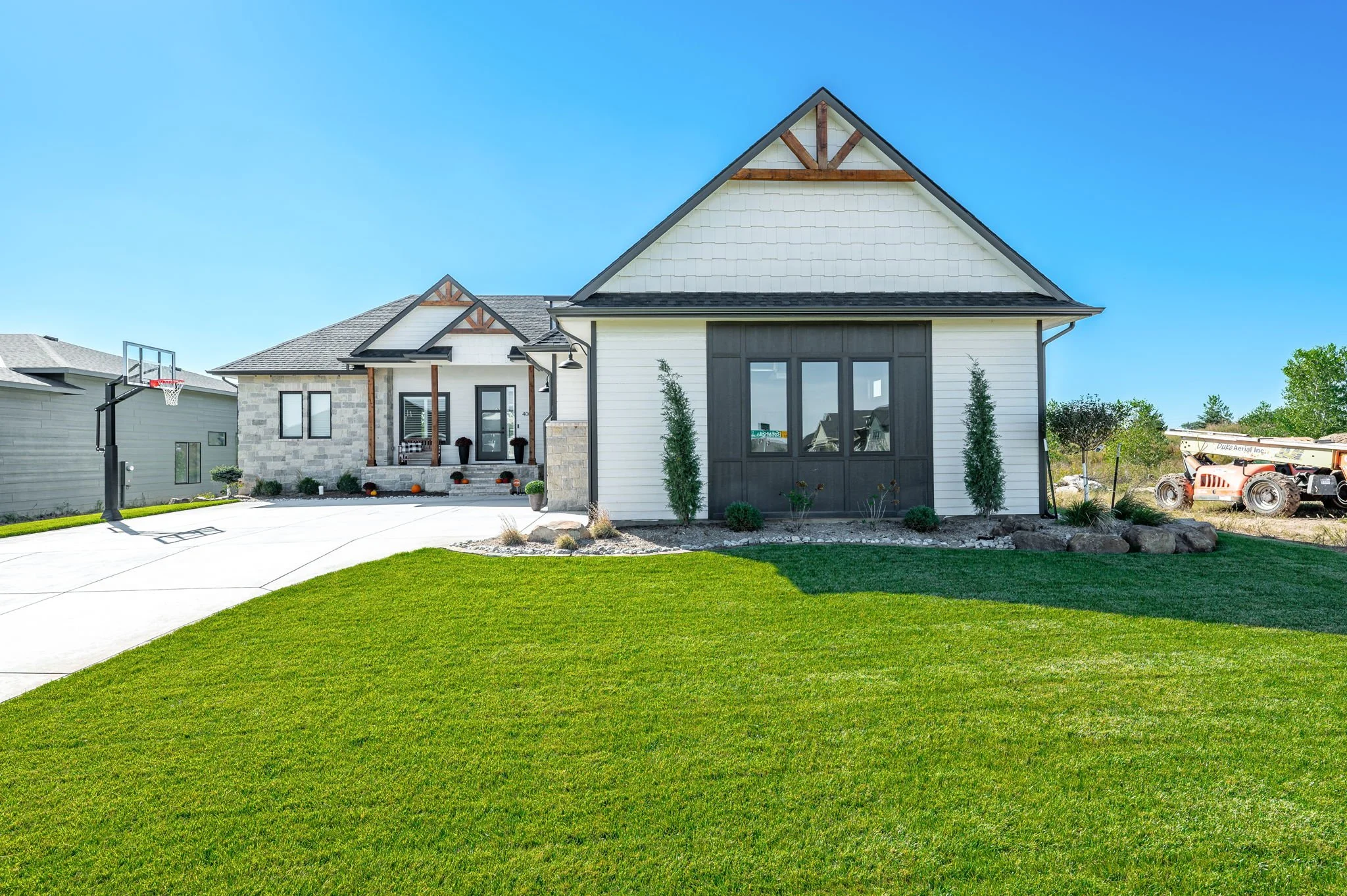 Modern two-story house with a white exterior, black window frames, and a gabled roof, situated on a lush green lawn under a clear blue sky.