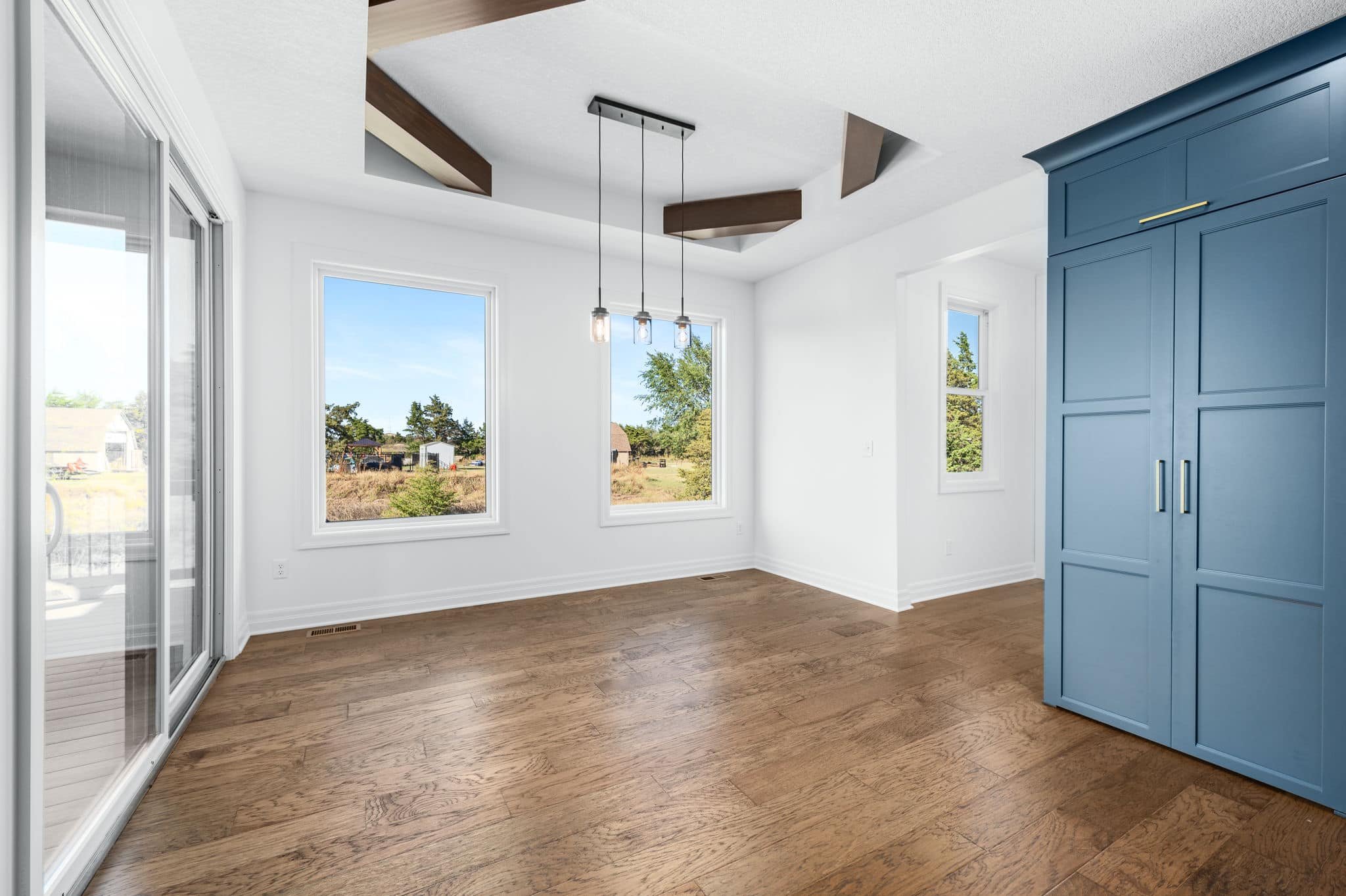 Empty room with large windows, hardwood floors, a blue cabinet, and a ceiling light fixture.