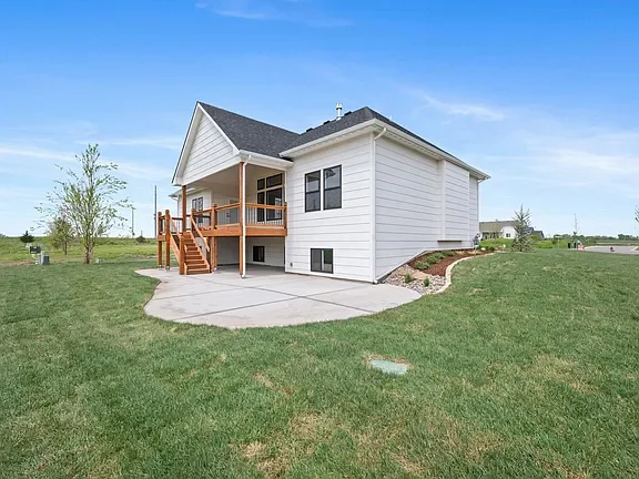 A white house with a pitched roof and a wooden deck, surrounded by a grassy yard and a clear blue sky in the background.