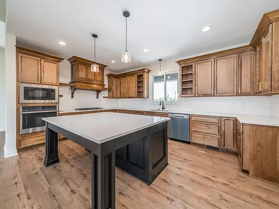 Empty kitchen with wooden cabinets, white countertops, and a central island with a dark base.