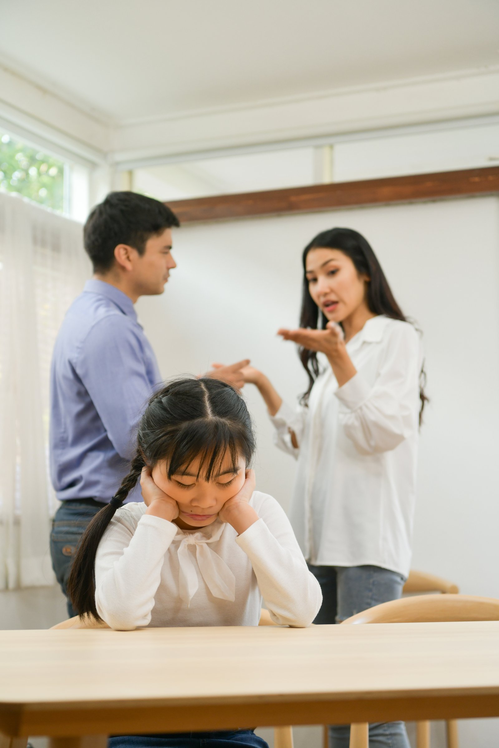 Image of an upset girl with arguing parents in the background.