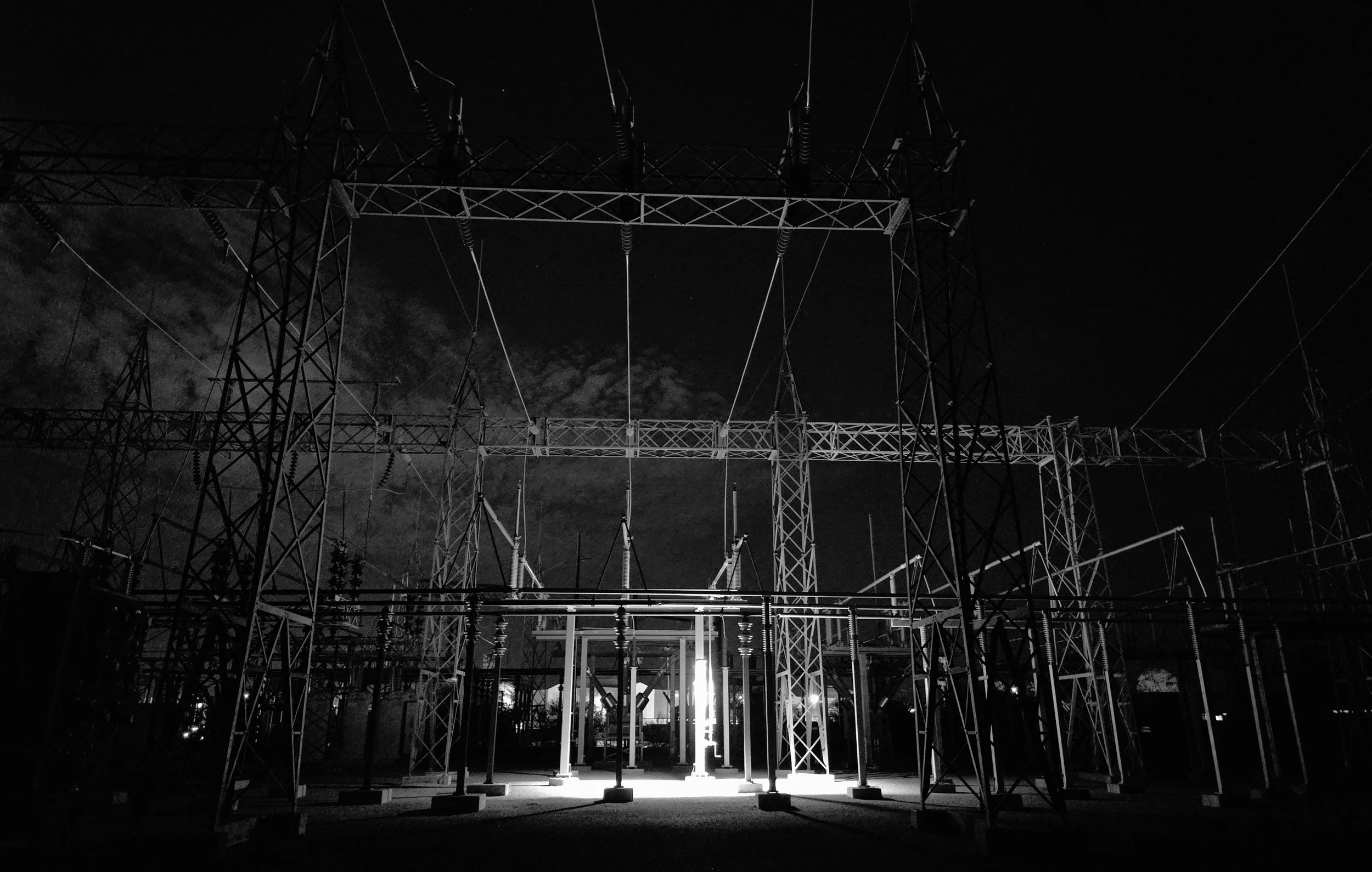Nighttime view of an electrical substation with power lines and towers illuminated by bright lights