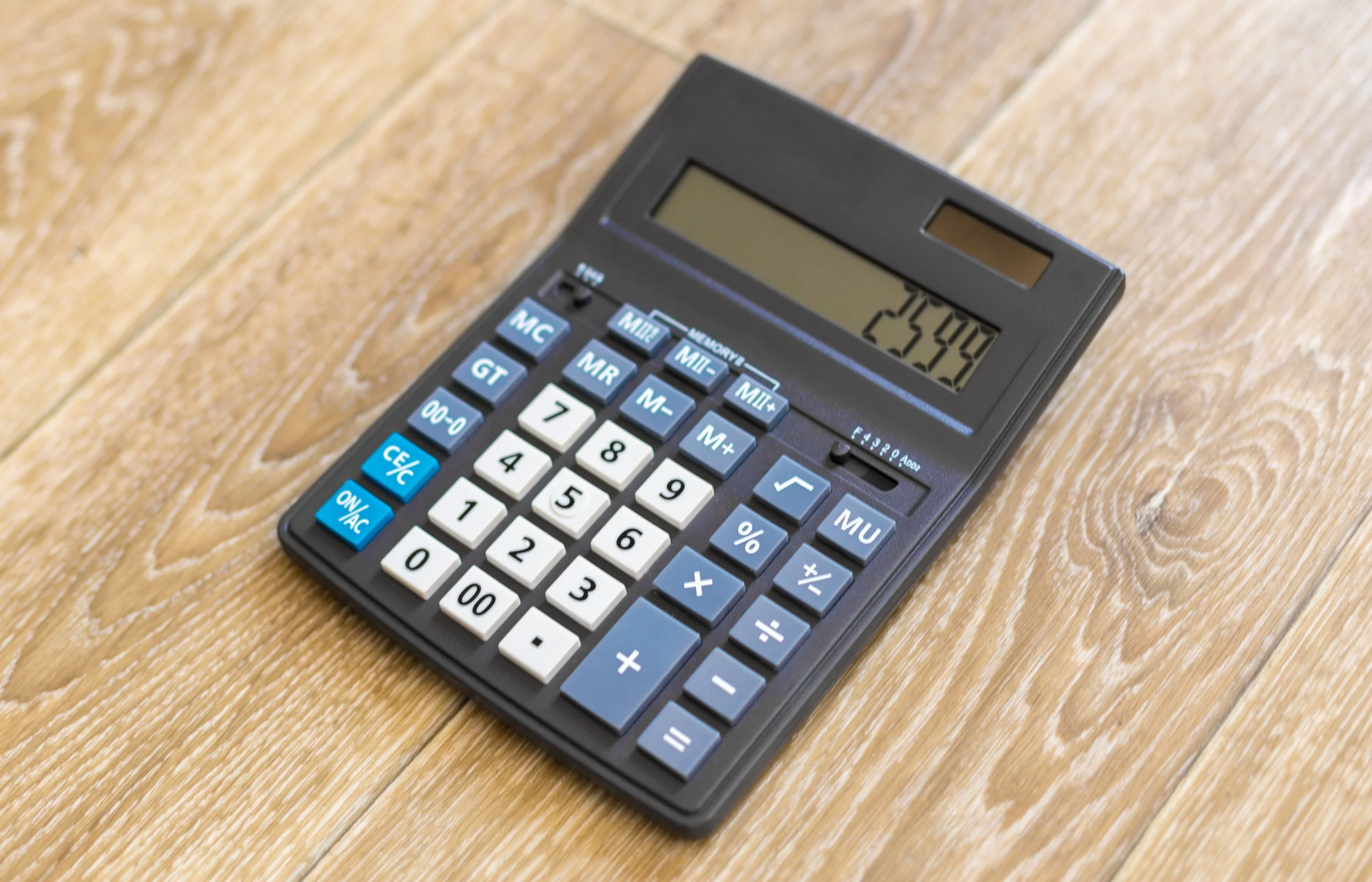 A black calculator with white and blue buttons displaying a total of 254.0 on its screen, placed on a wooden surface.