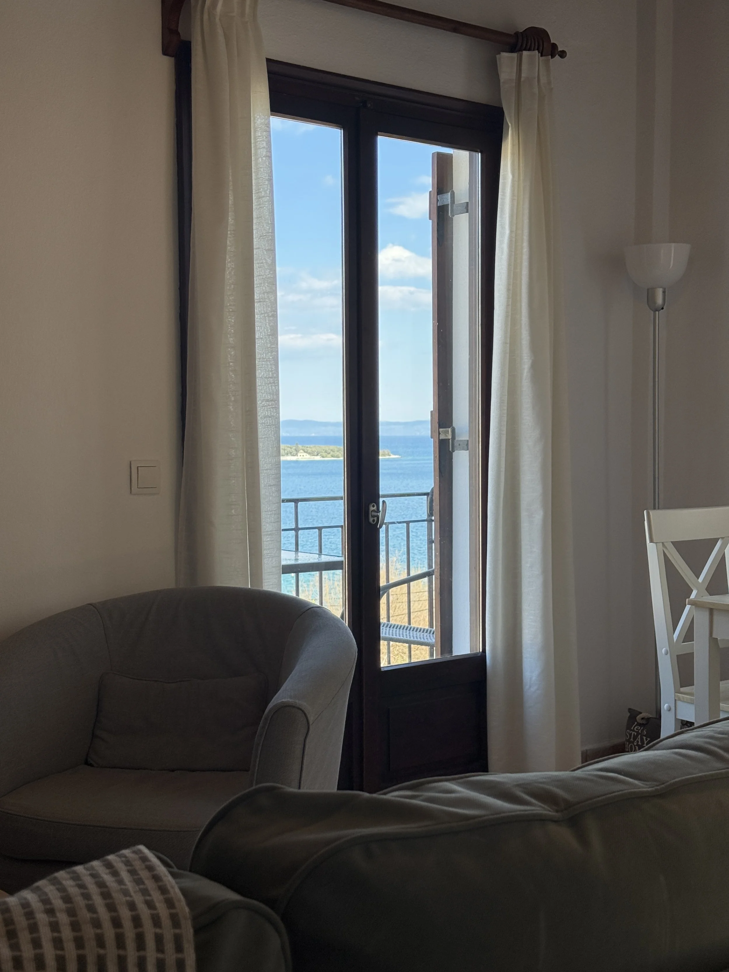 Living room with beige sofas, a glass door opening to a balcony, and a view of the water and sky outside.