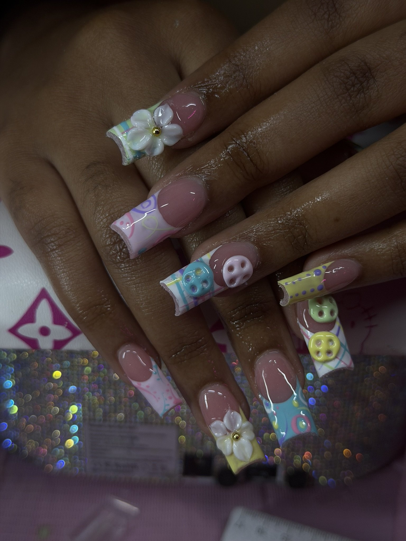 Close-up of decorated nails with colorful, pastel designs featuring buttons and flowers.