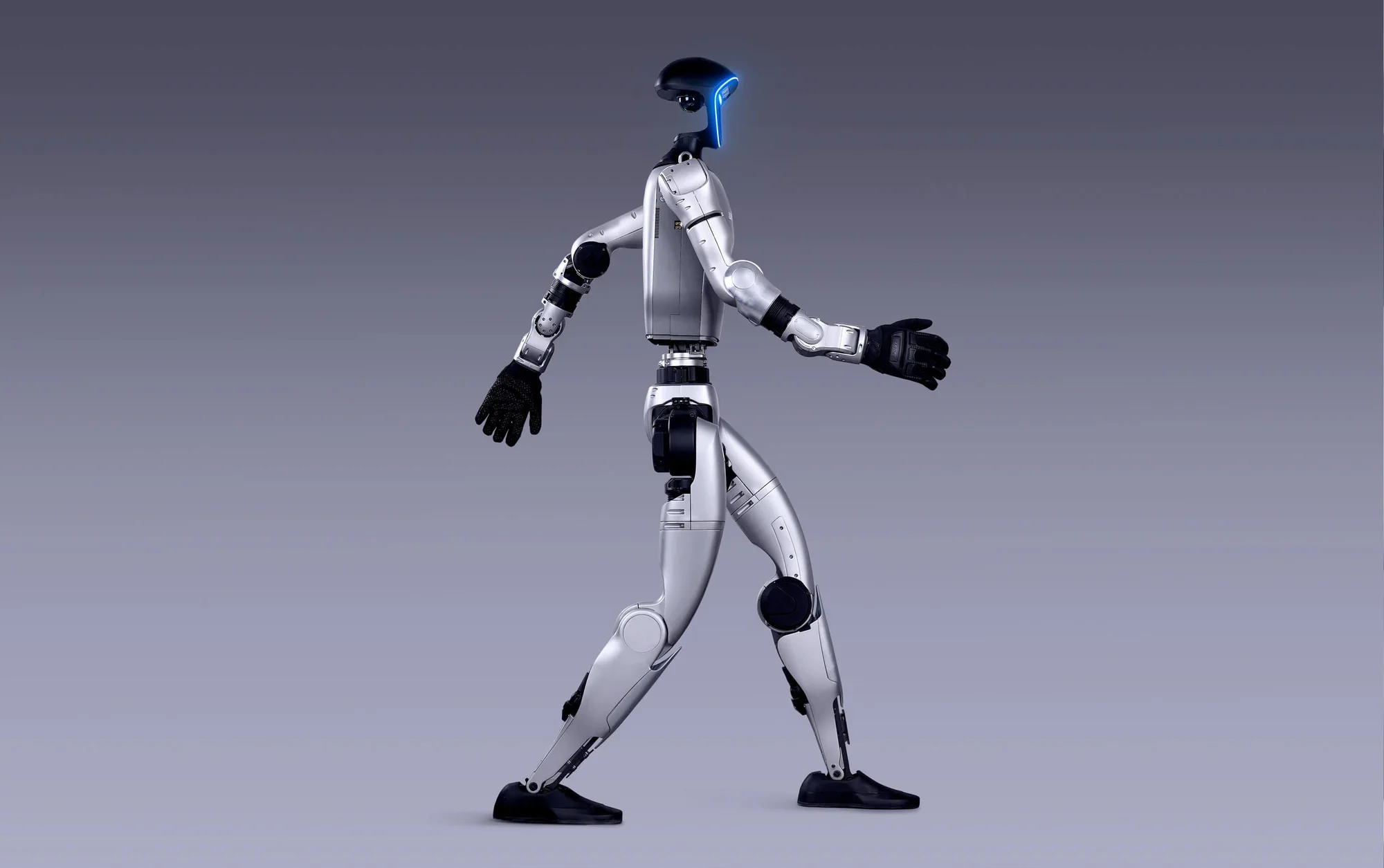 A humanoid robot with a sleek, futuristic design and a black and silver color scheme walking against a plain gray background.