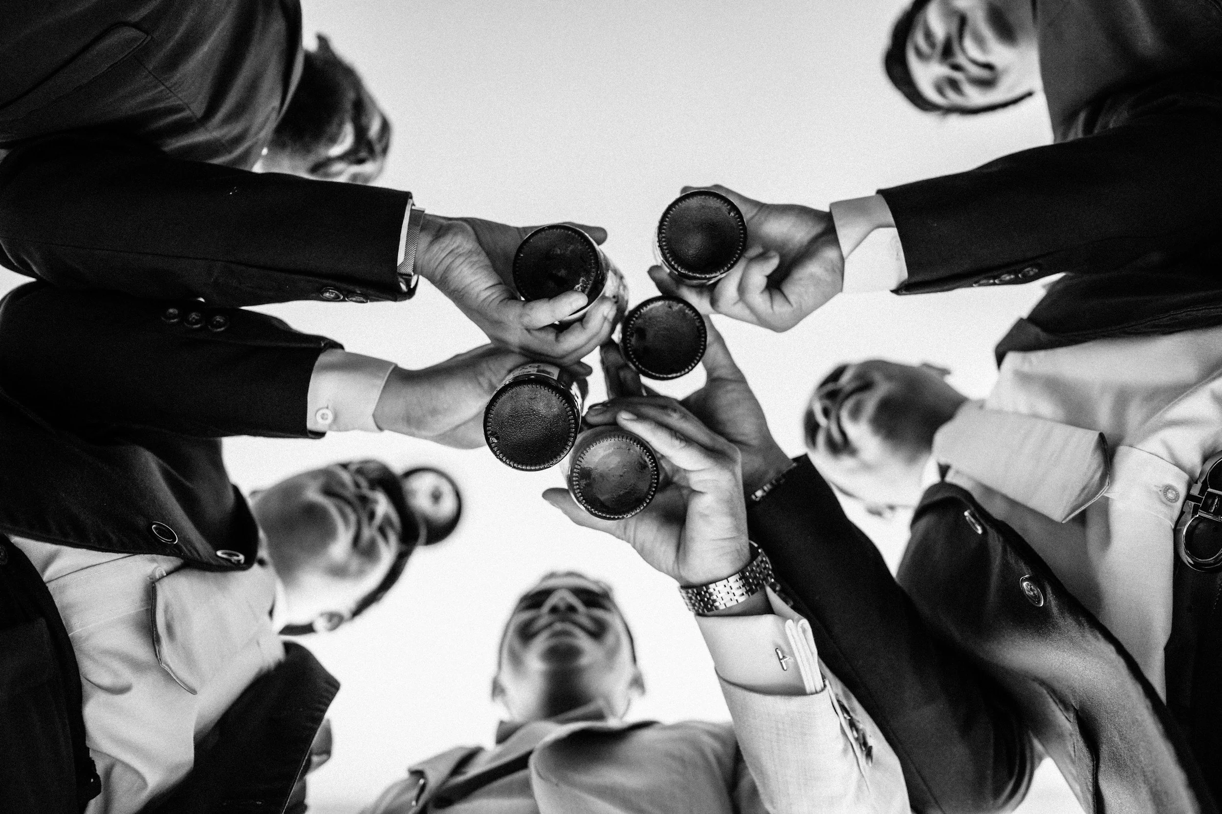 People in business suits clinking beer bottles together in a circle as viewed from below.