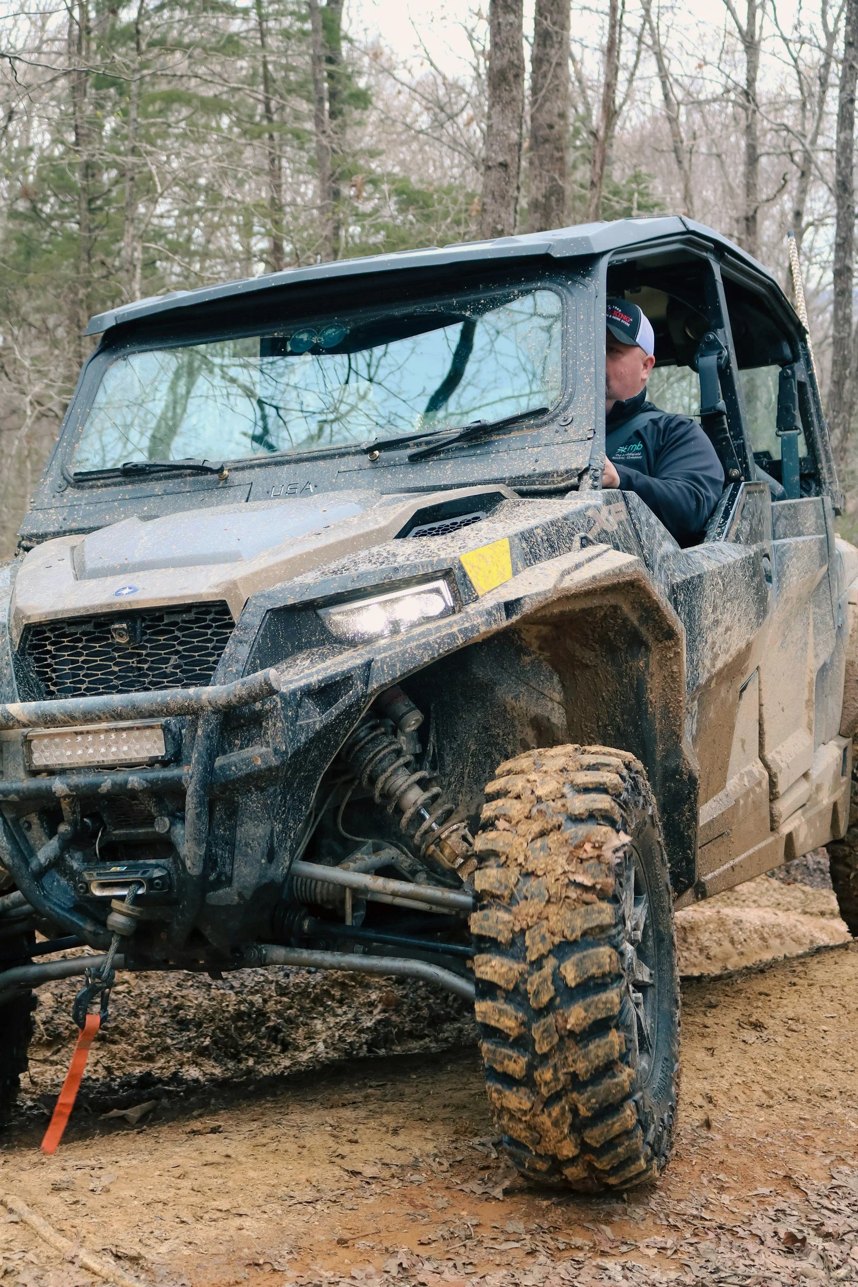 A man driving a rugged off-road vehicle on a muddy trail in a forested area.