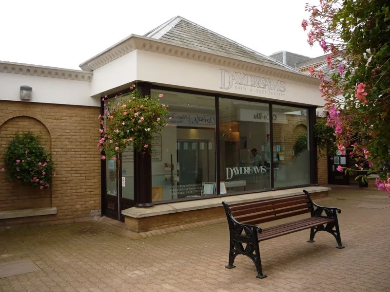 storefront with glass windows, potted flowers, a bench outside, and a sign that reads 'DAYDREAMS SKIN & BEAUTY'