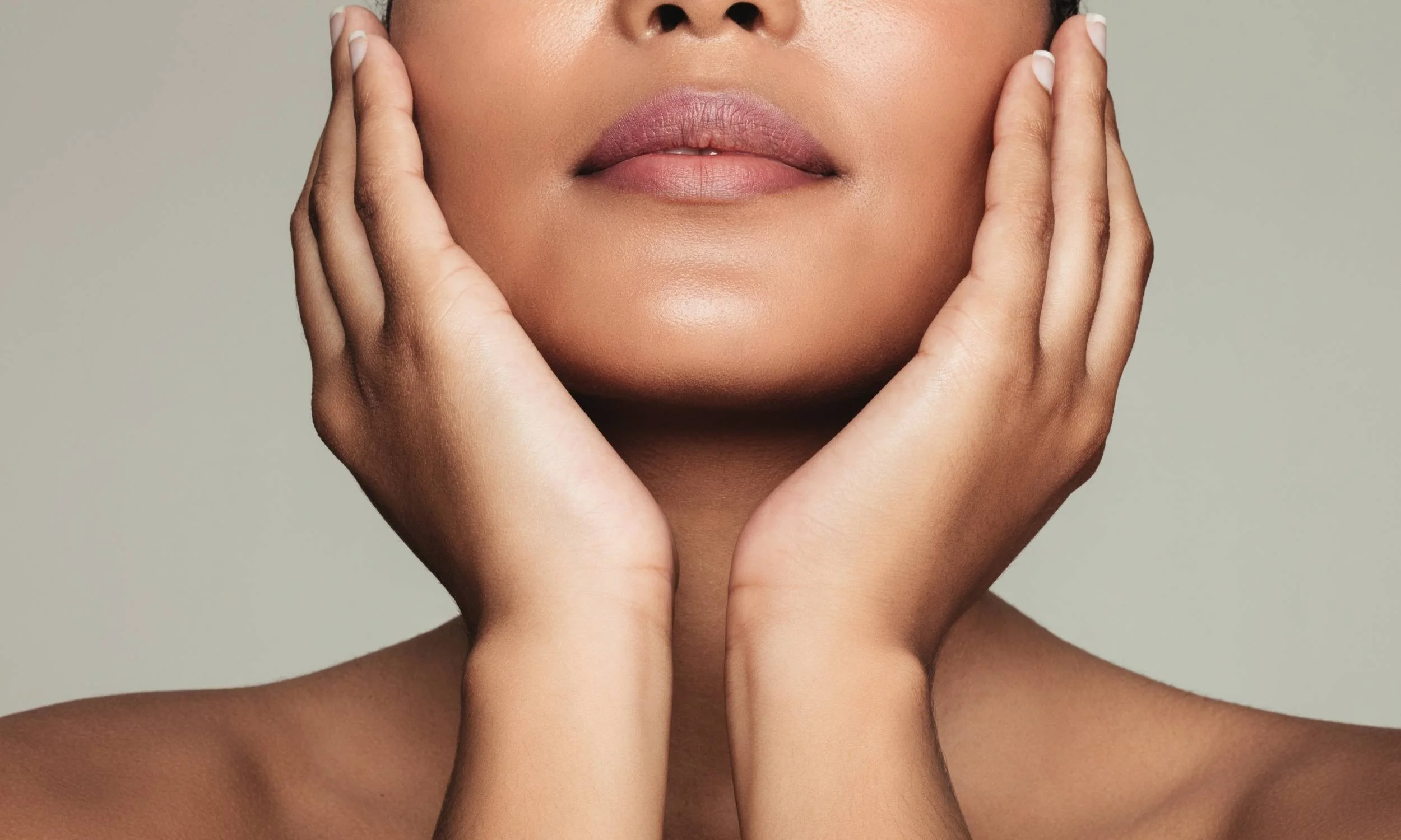 Close-up of a woman with hands framing her face, focusing on her lips and part of her face, with smooth skin and natural makeup.