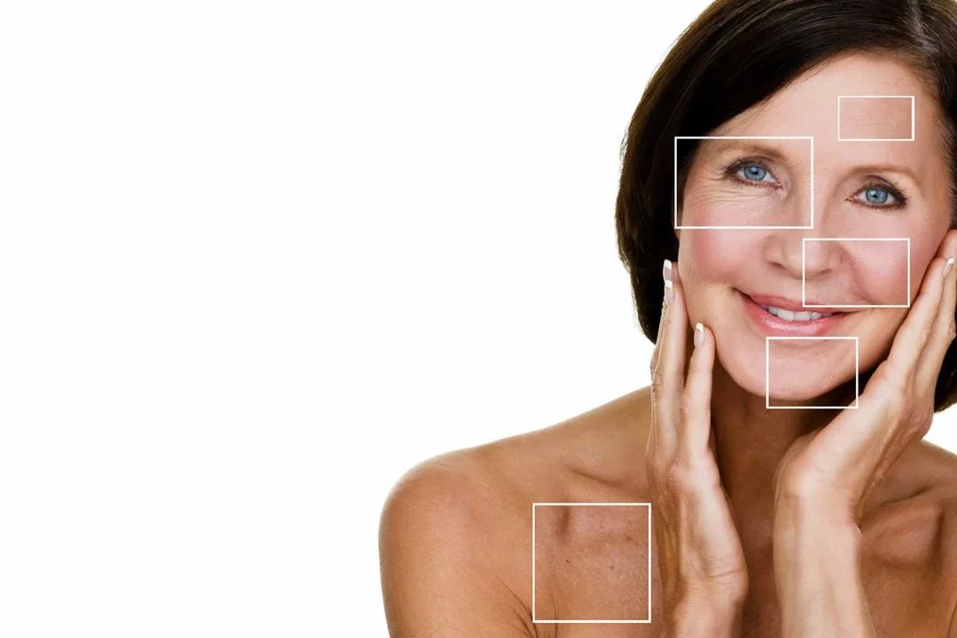 A woman touching her face with her hands, smiling, with highlighted sections on her face and shoulder indicating focus points, against a white background.
