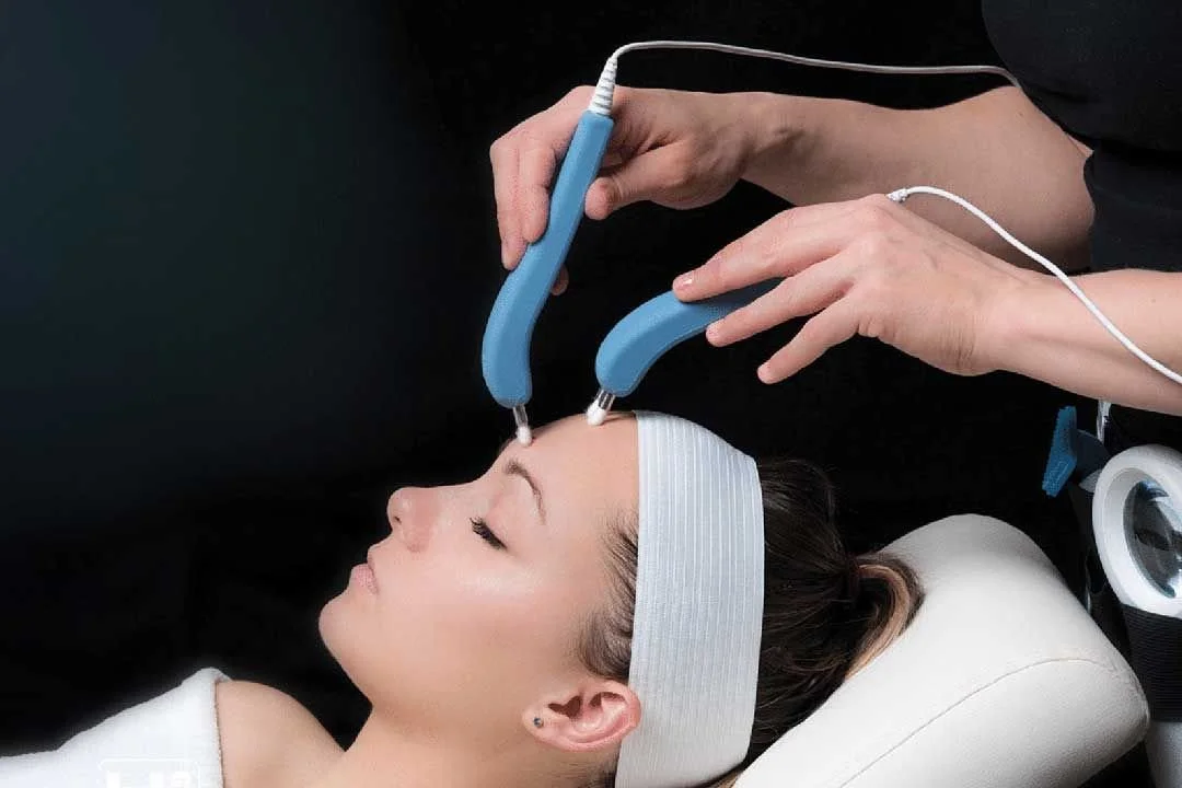 A woman receiving a facial treatment with ultrasonic skin scrubber devices held by a practitioner.