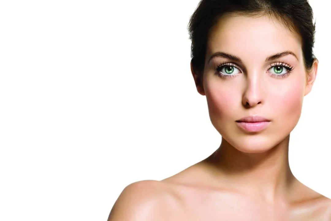 Close-up of a young woman with short dark hair, bright blue eyes, and clear skin against a white background.