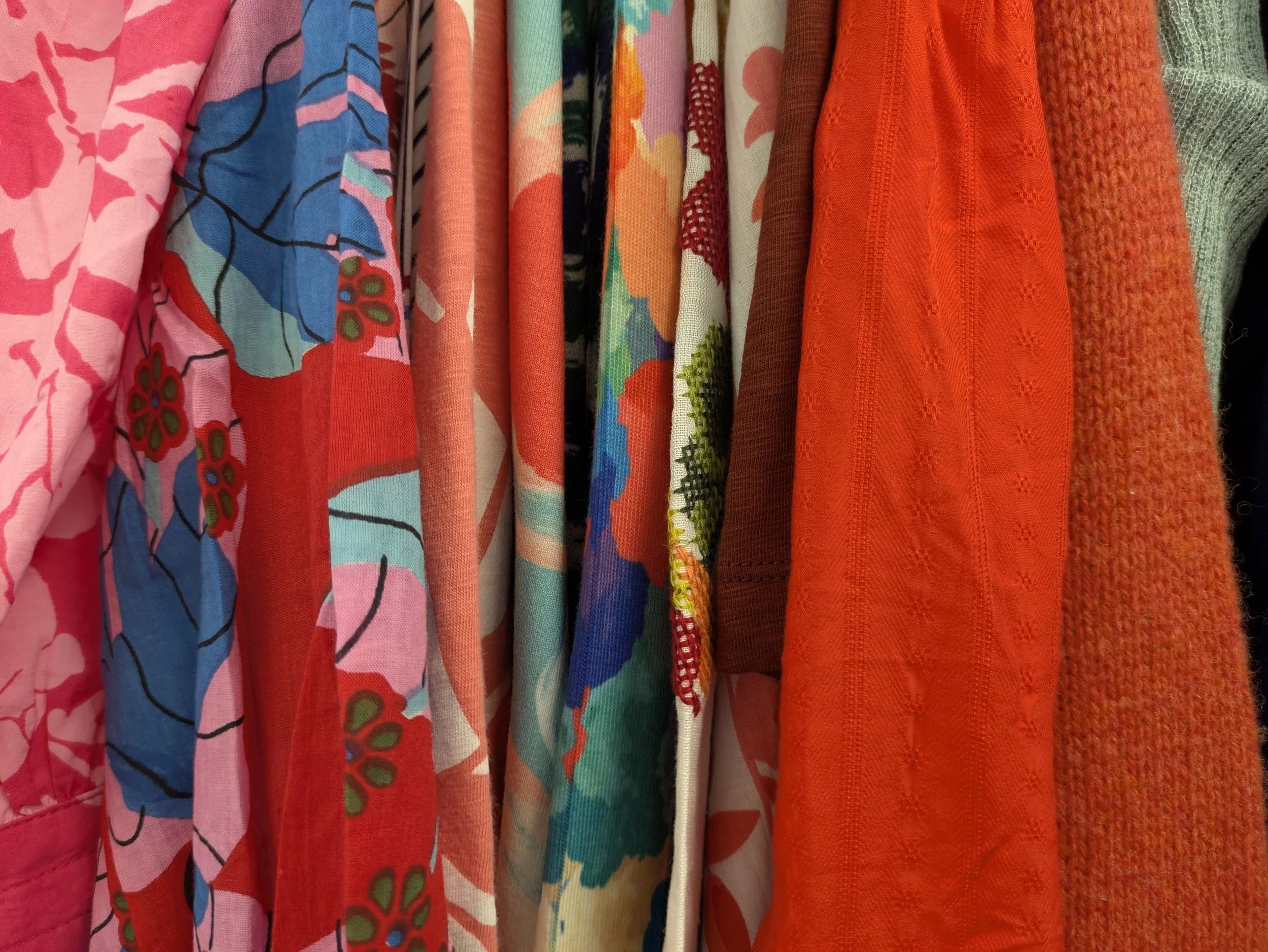 Colorful hanging towels or fabrics with various floral and abstract patterns in shades of pink, blue, red, green, orange, and cream. The Lucky Penny Consignment East Granby, CT