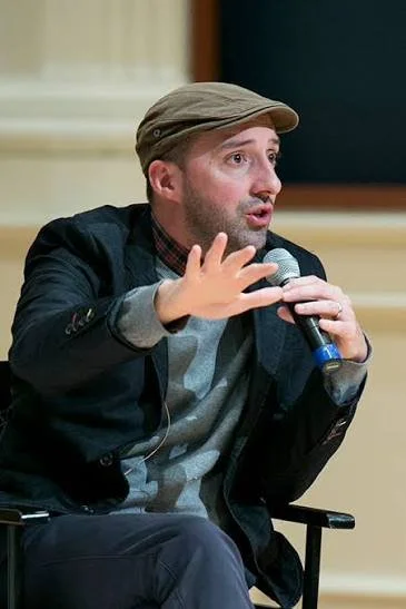 Tony Hale speaking into a microphone during a discussion or presentation.