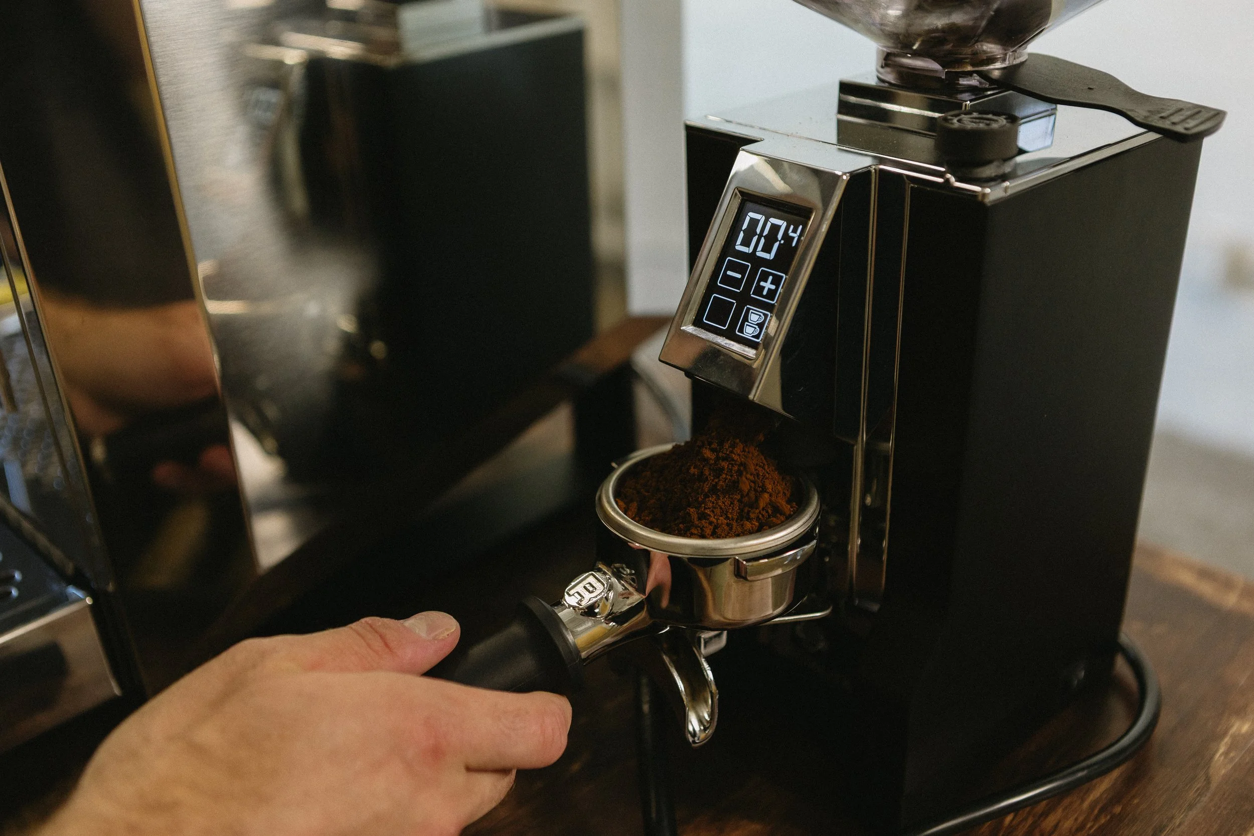 A person is using a coffee grinder to grind coffee beans, with a container filled with ground coffee underneath.