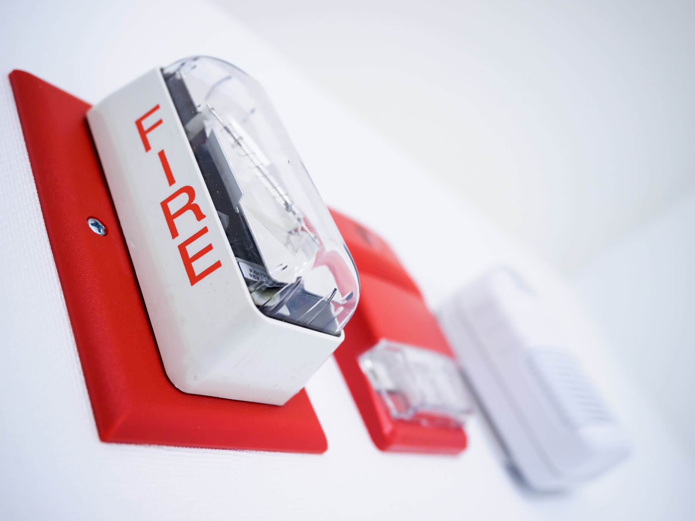 Close-up of a red and white fire alarm with an open transparent cover, mounted on a white wall.
