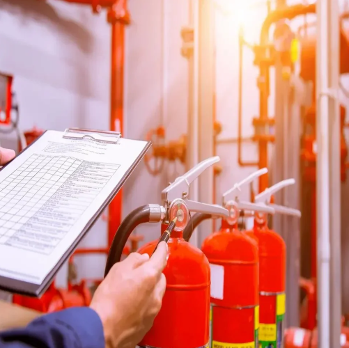 Person inspecting fire extinguishers in a fire safety room with red piping.