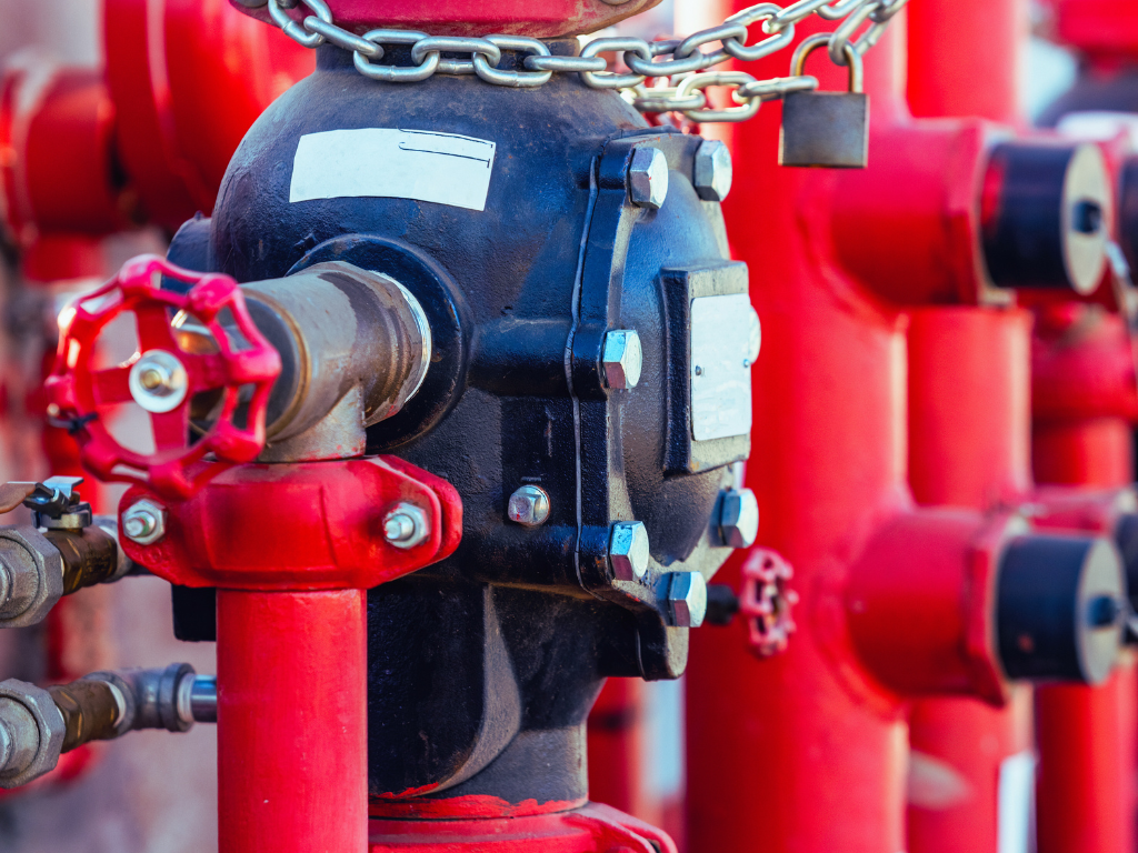 Close-up of industrial pipes, valves, and equipment painted in red and black, with chains and bolts visible.