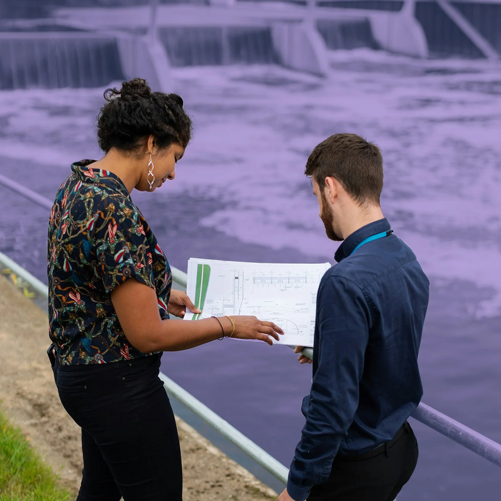 Two engineers review plans near a hydroelectric dam