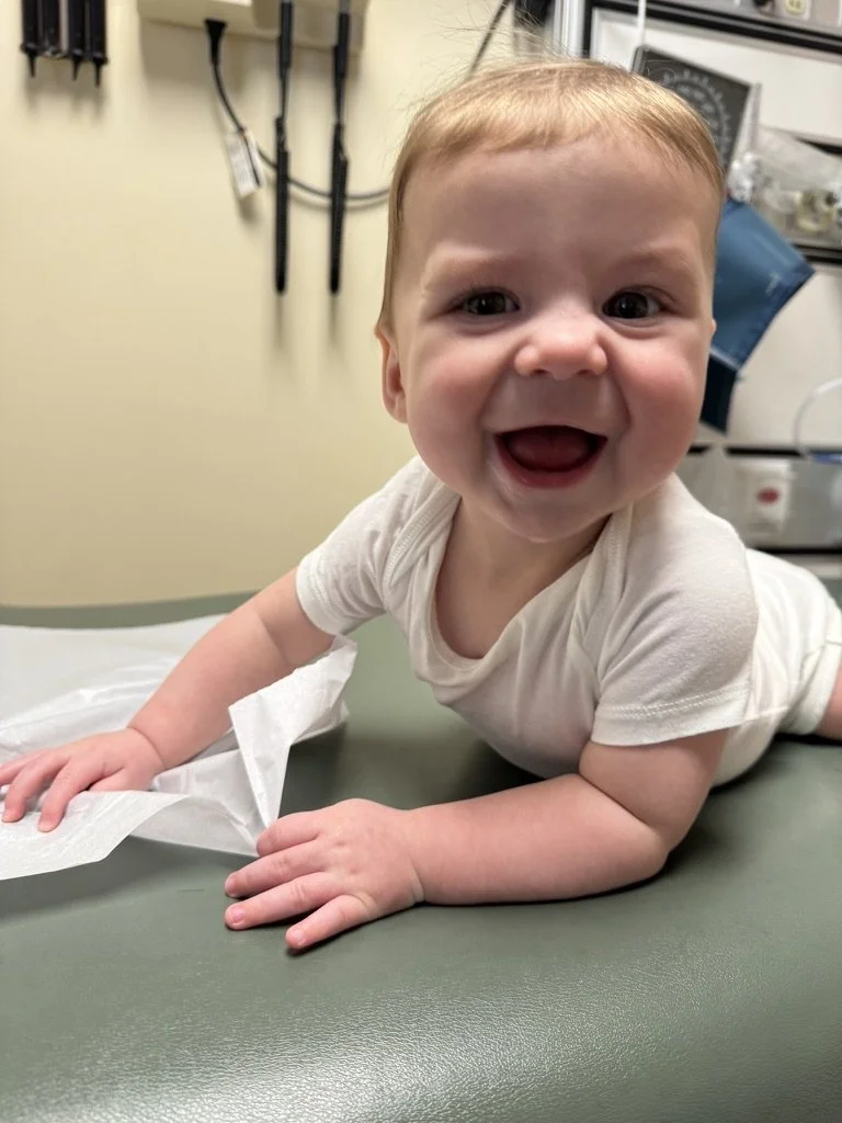 Happy baby lying on a medical examination table in a clinic, smiling at the camera.