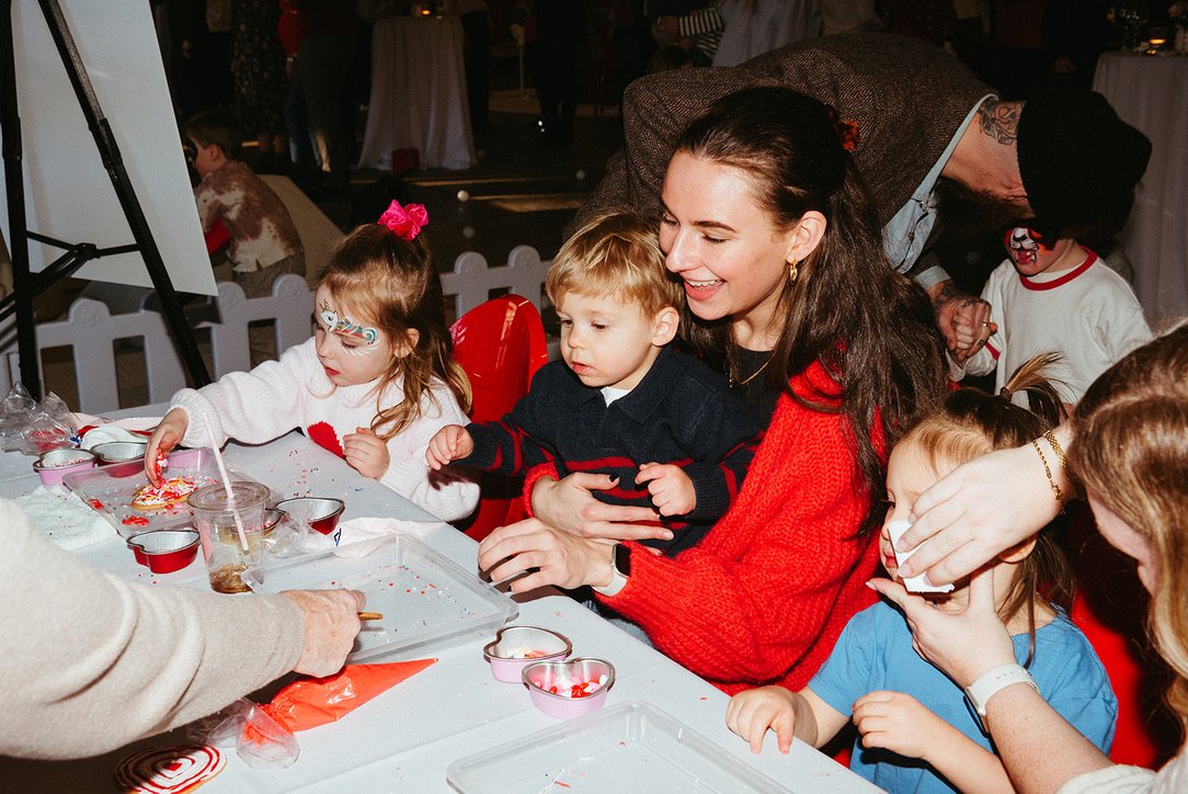 A group of children and adults enjoying a party, making and decorating cookies at a table with various supplies.