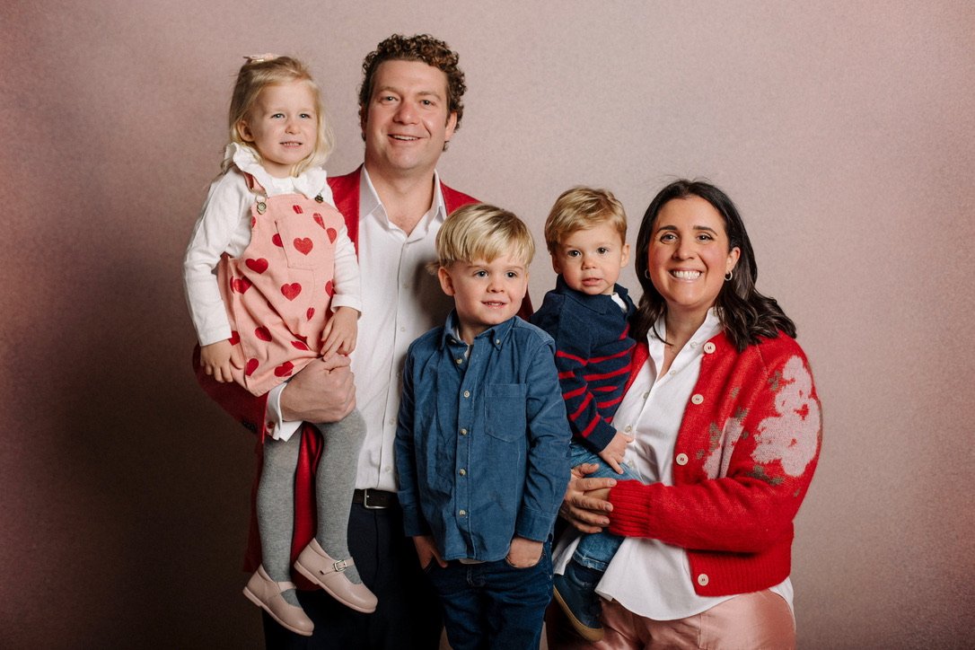A happy family of five posing together against a plain background, with children and adults smiling and wearing casual winter clothing.