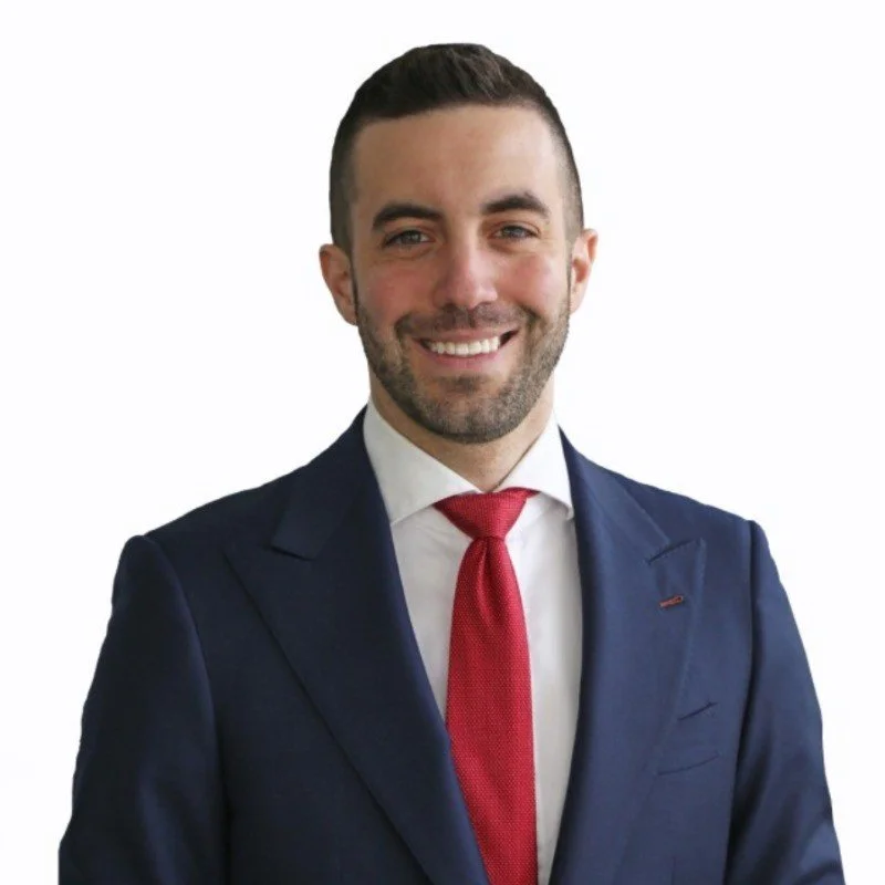 A smiling man in a navy blue suit, white shirt, and red tie posing against a white background.