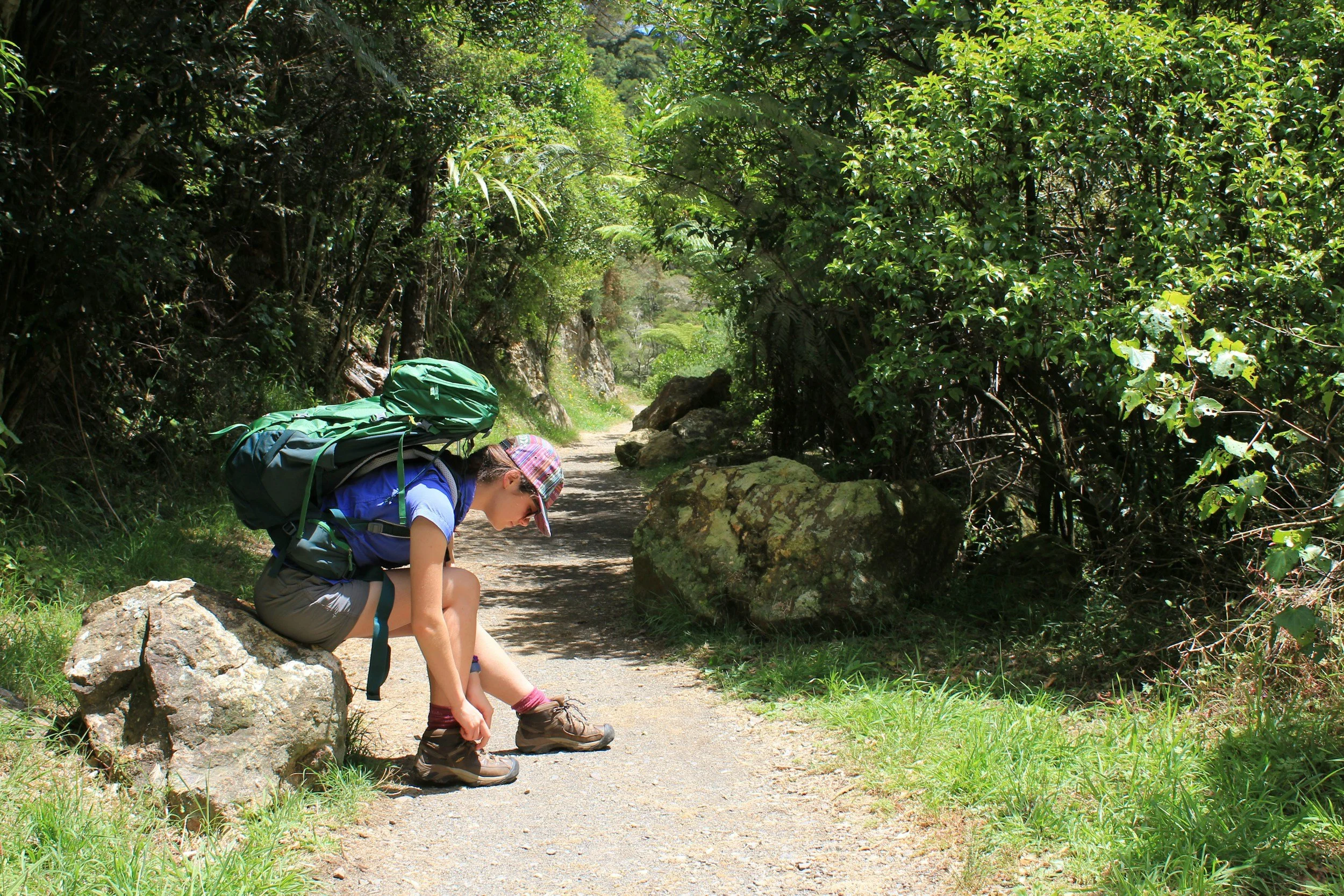 A person sitting on a rock on a forest trail, tying their hiking boots.
