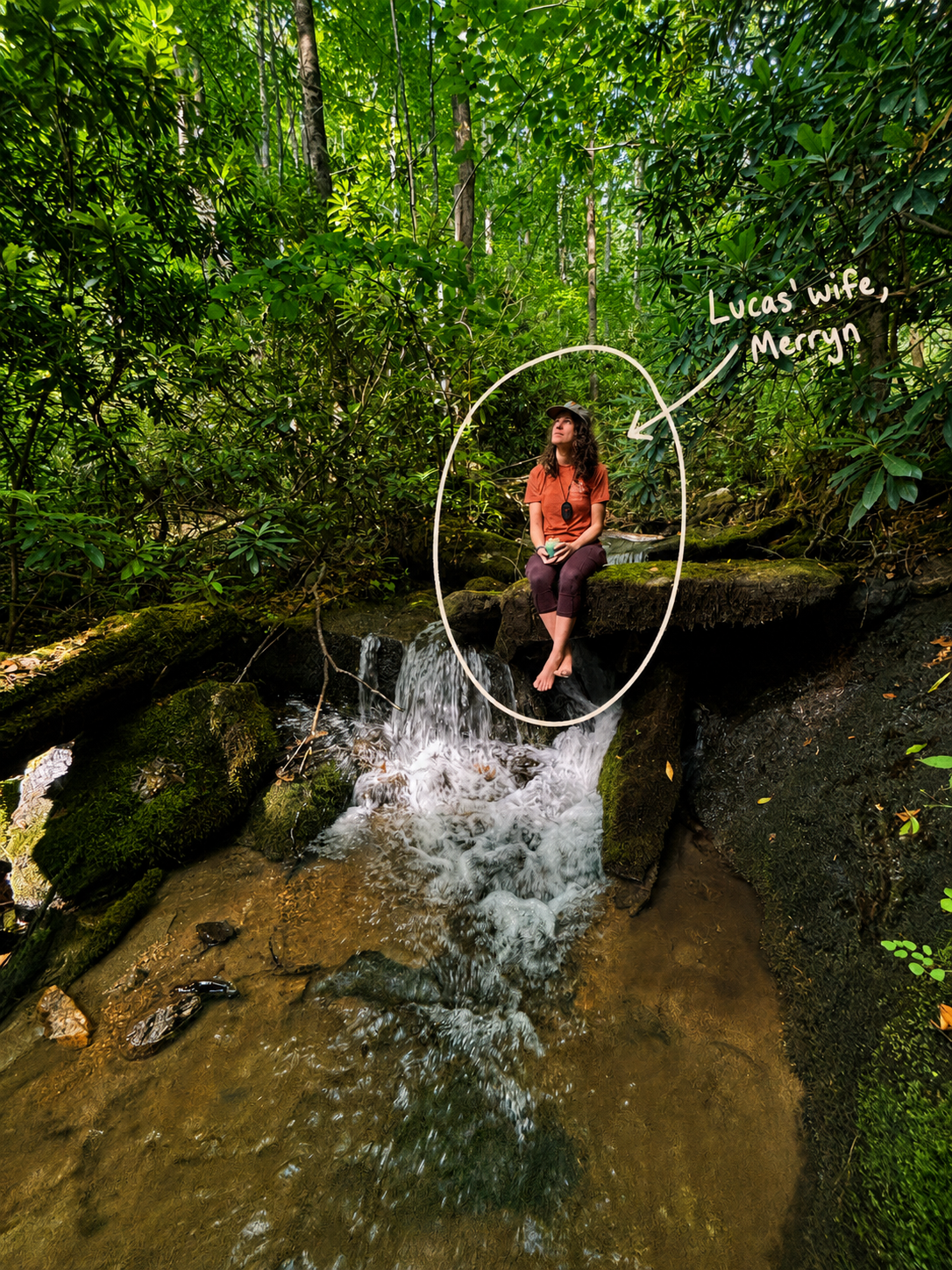 A woman sitting on a mossy rock ledge over a small stream in a lush green forest, with a handwritten note pointing to her that says 'Lucas wife, Meryn'.