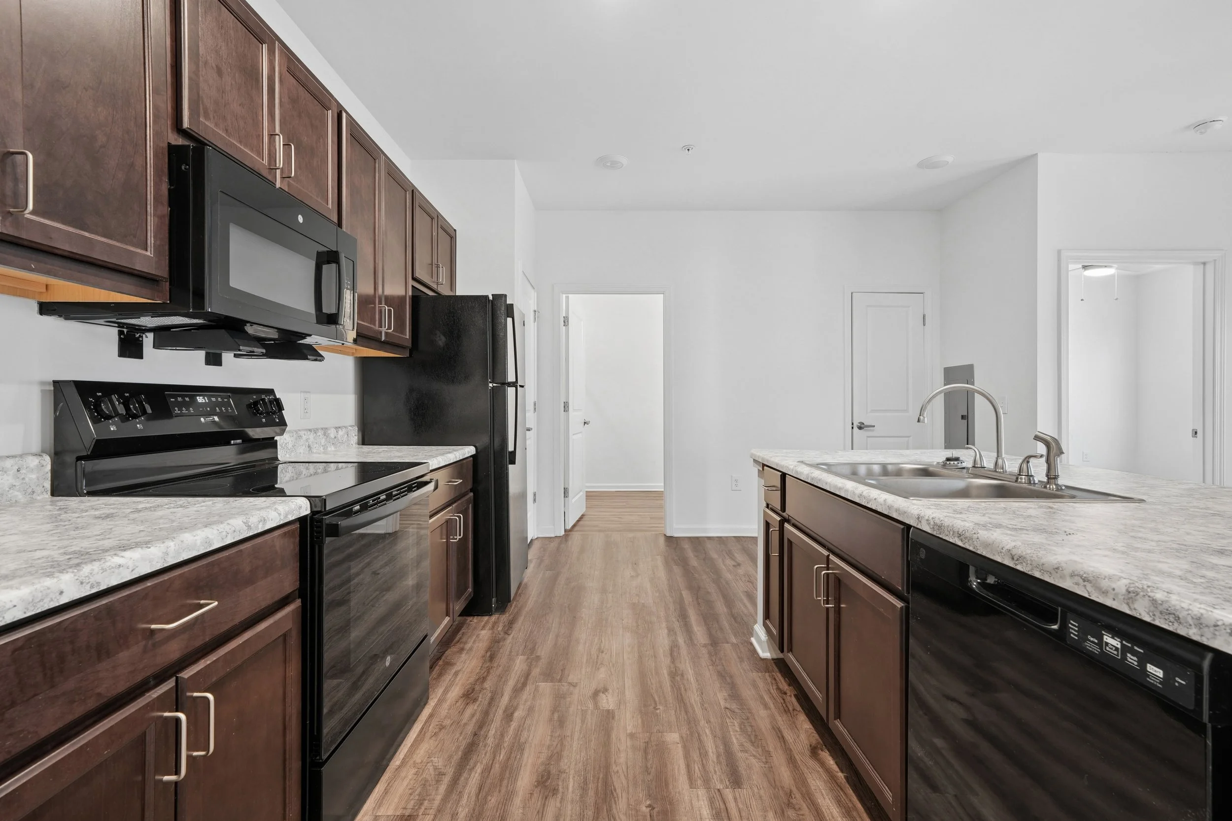 Kitchen with dark wood cabinets, light countertops, and black appliances including a microwave, refrigerator, and stove. There is a double sink and a hardwood floor.