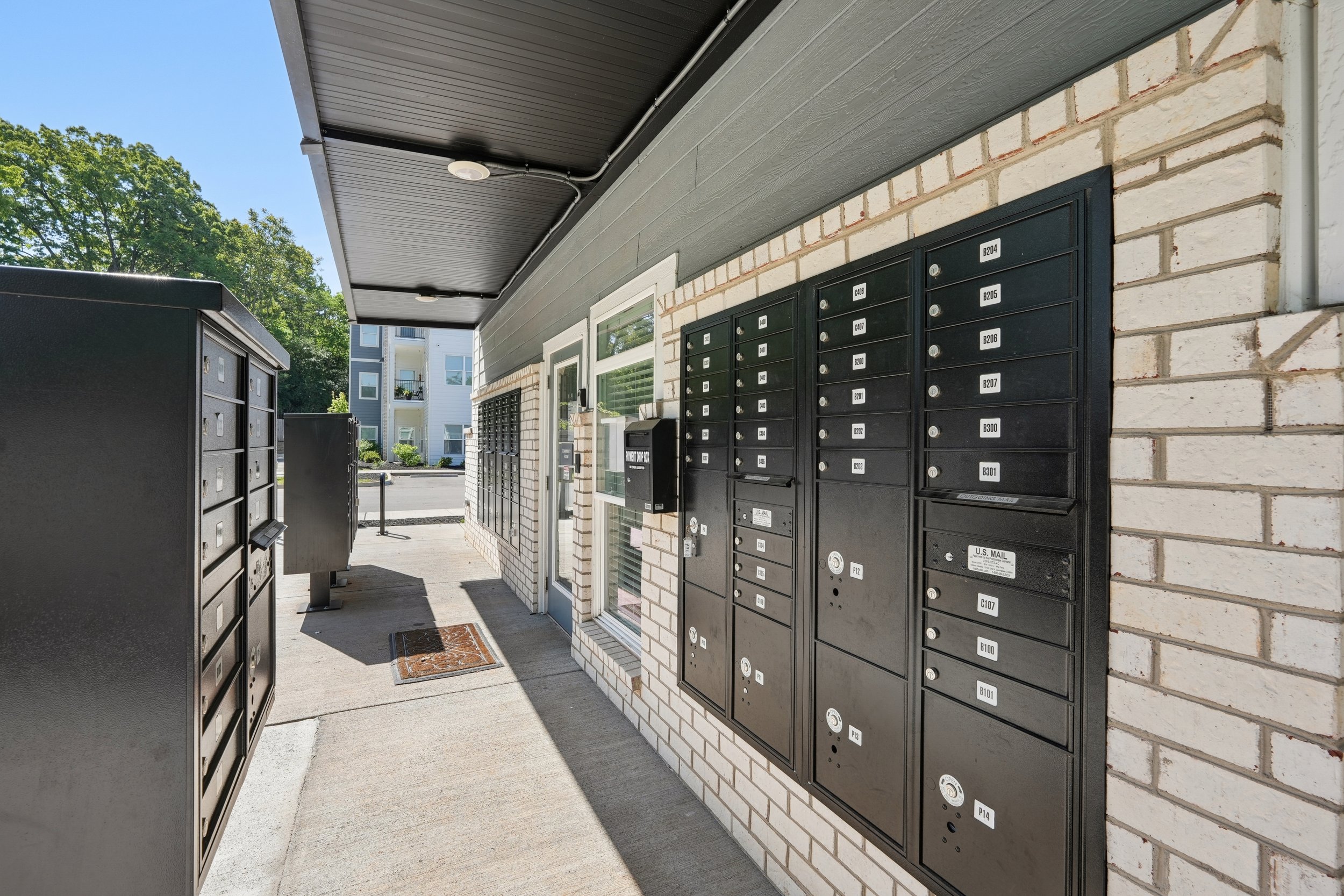 Apartment building entrance with black mailboxes mounted on a brick wall, glass door, and a concrete sidewalk.