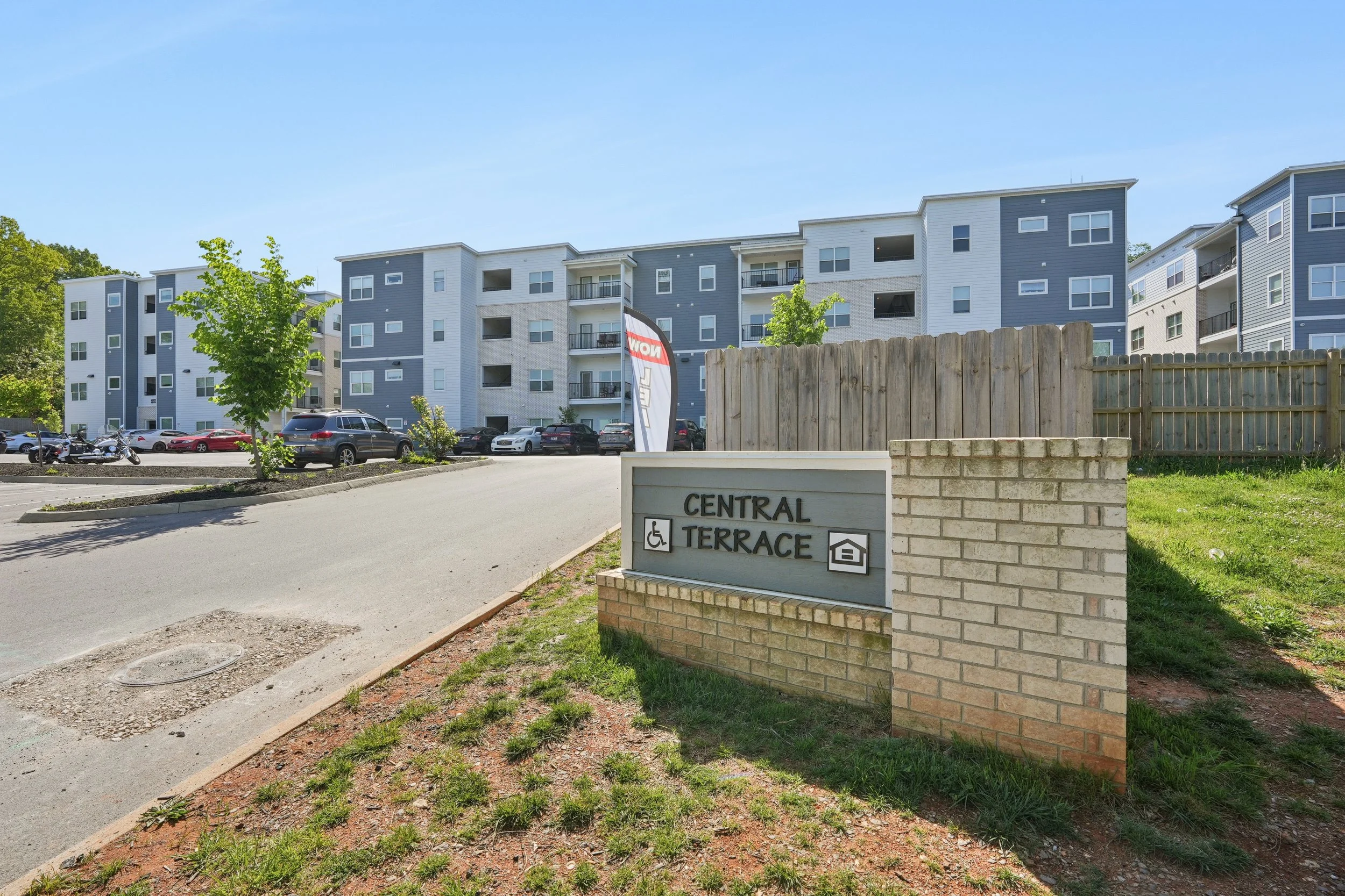 View of a modern multi-story apartment complex with a parking lot in front, some parked cars, and a sign indicating the name 'Central Terrace' and wheelchair accessibility.