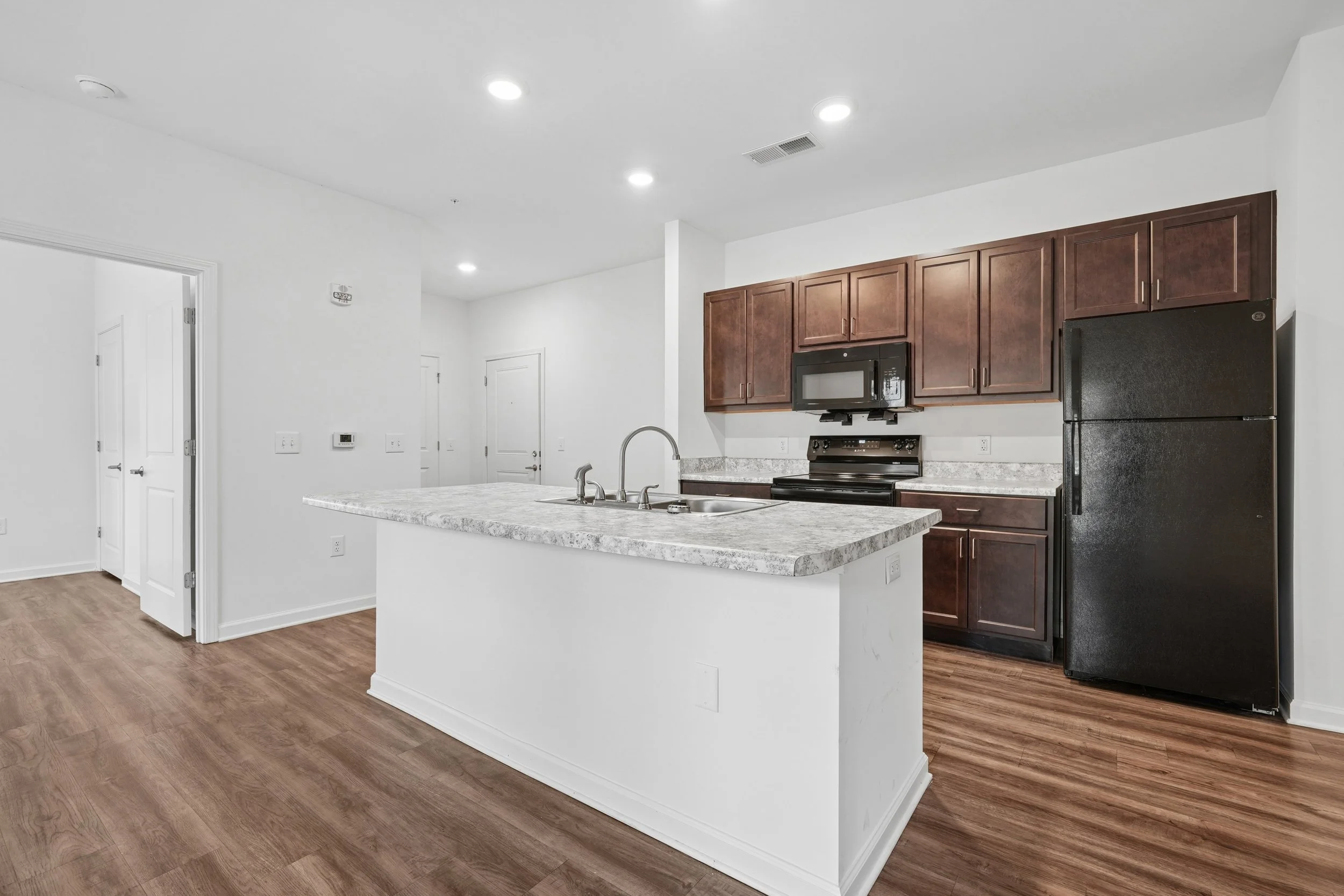 Modern kitchen with white walls, wooden cabinets, black appliances, granite countertops, and hardwood floors.