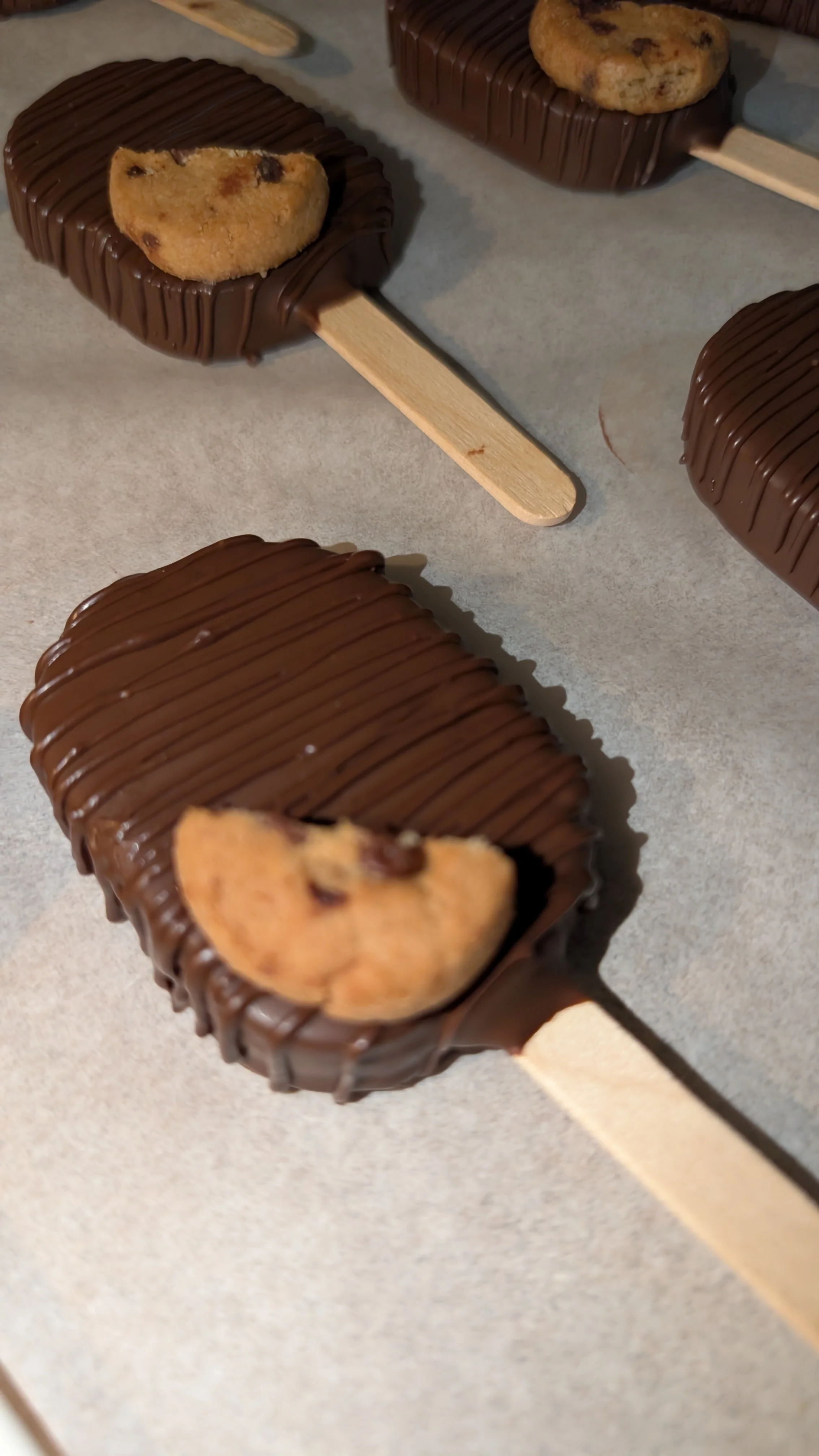 Chocolate chip cookie dough cake pop on wooden sticks with chocolate chip cookie halves on top.