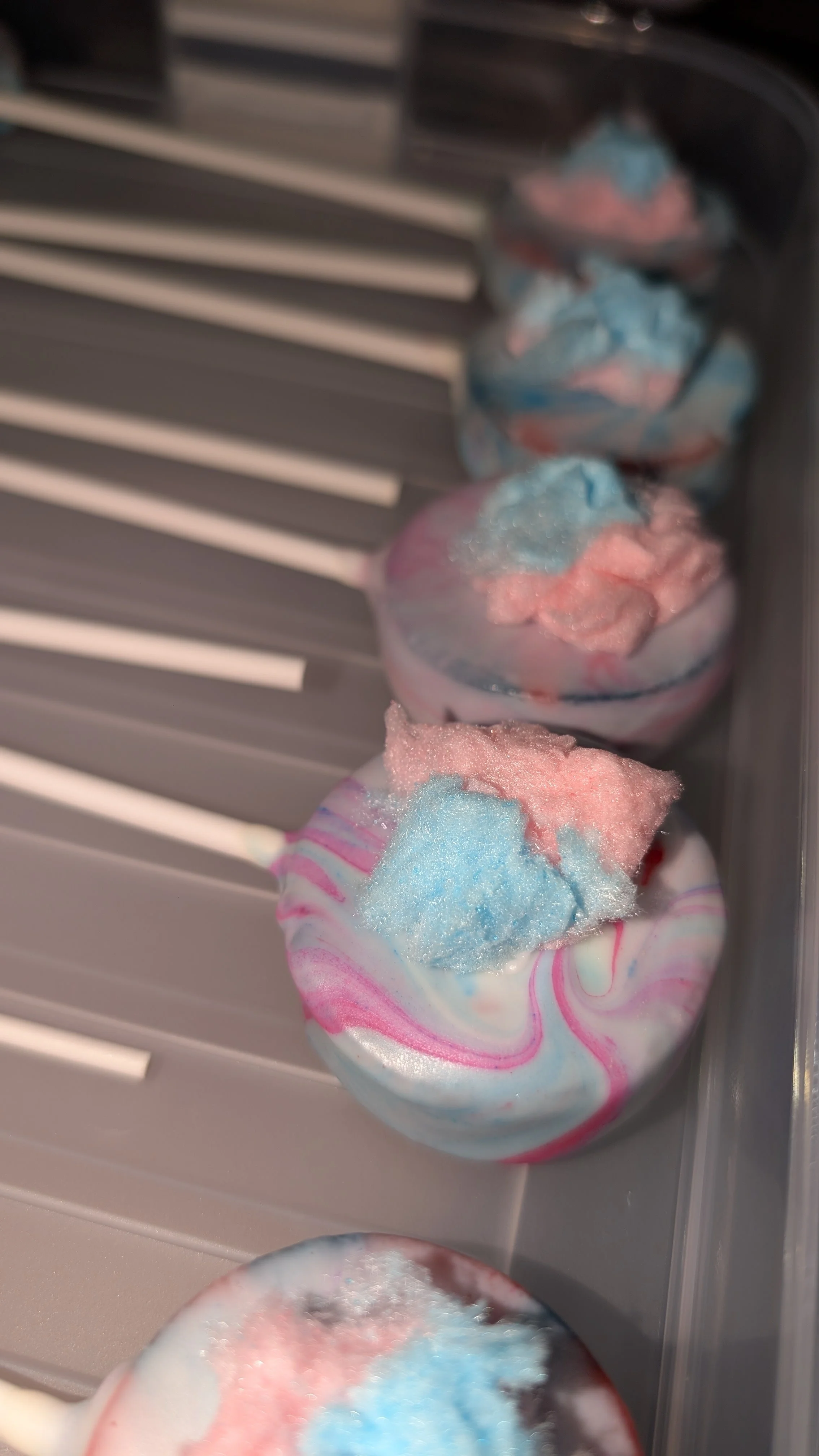 Colorful cotton candy with pink and blue swirls inside paper cups, aligned in a row.