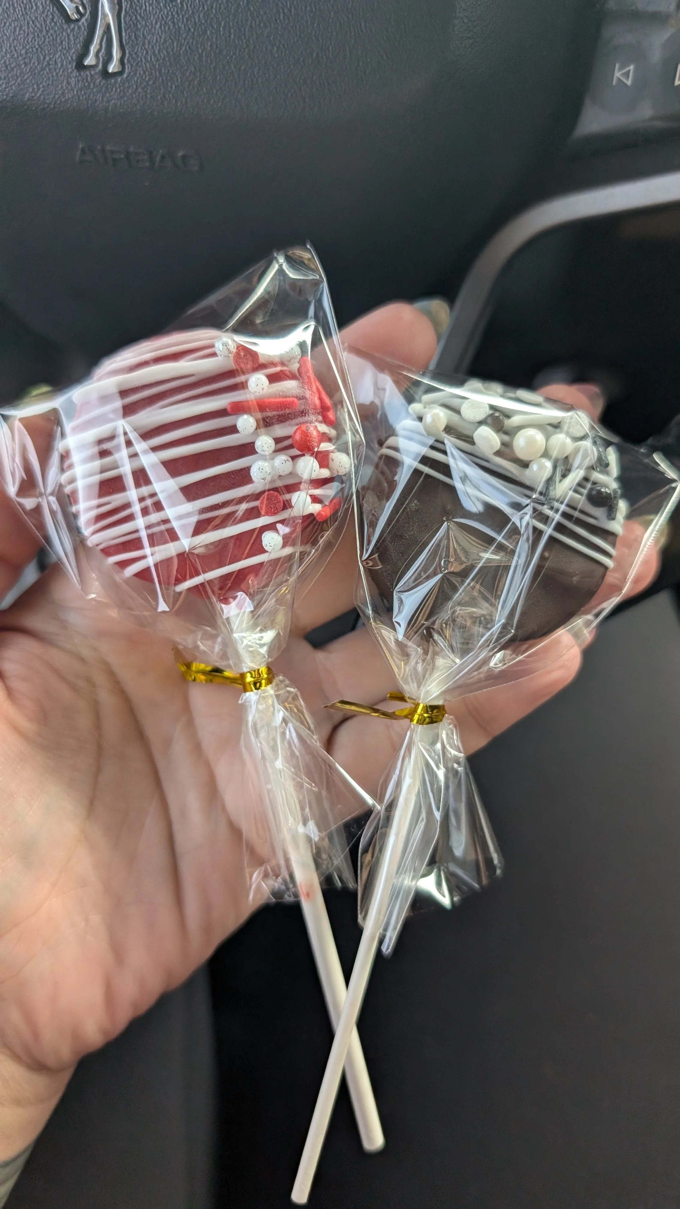 Two decorated cake pops, one with red and white stripes, and the other with white and black stripes, held in a hand with a black background.