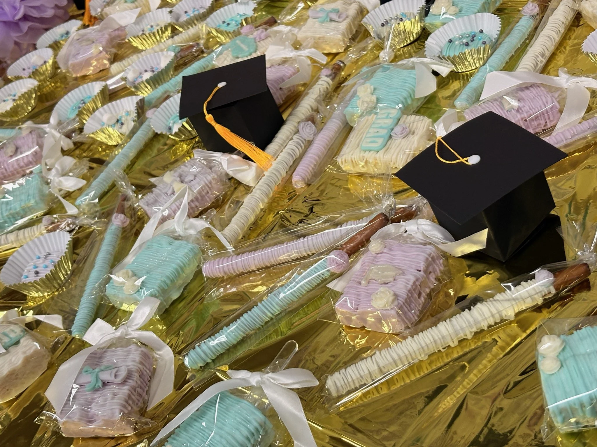 Assorted decorated treats wrapped in clear plastic and placed on a golden surface, some with graduation caps decorations.