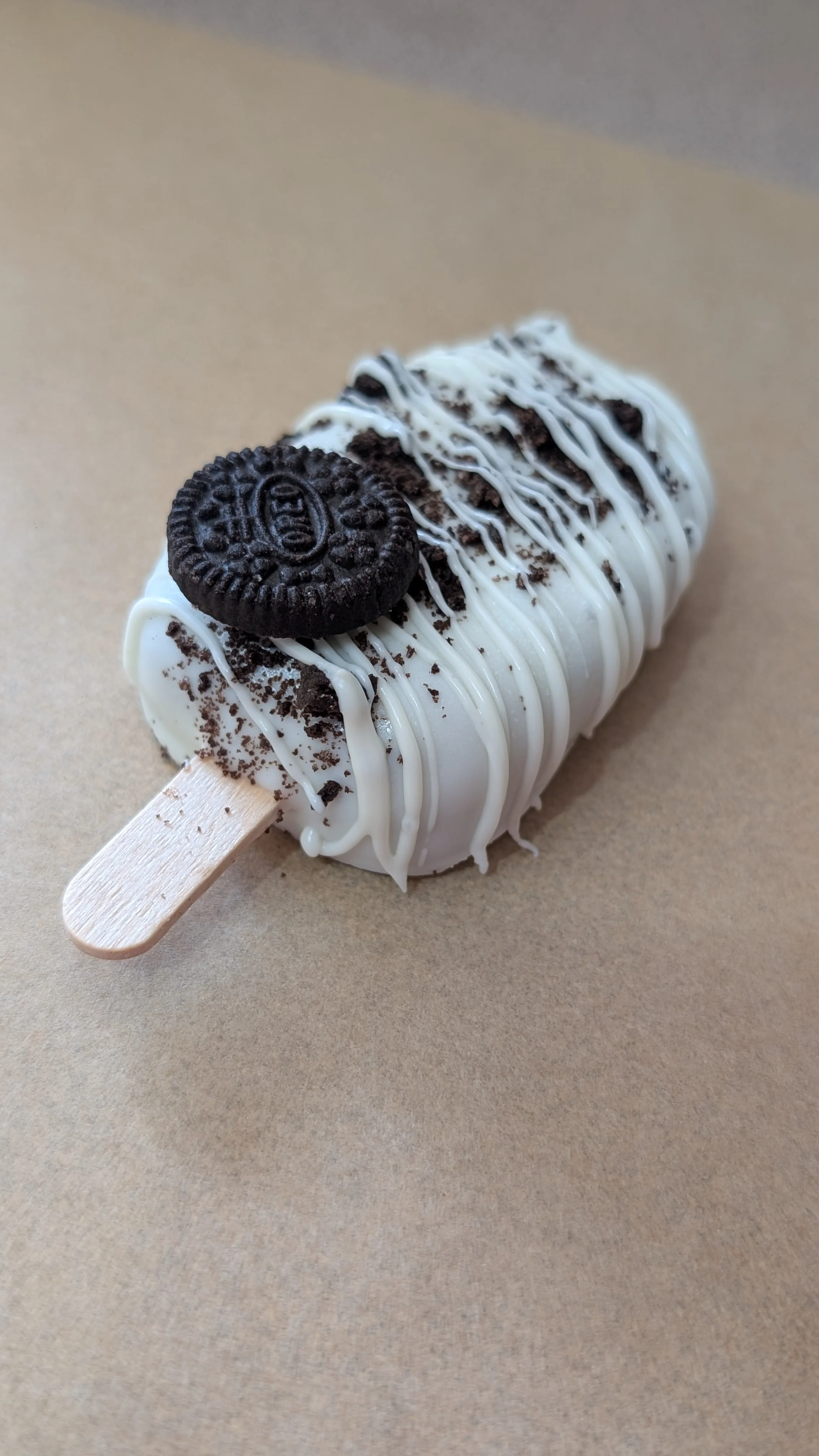 Oreo cookies and white chocolate coating on cakesicle with white chocolate drizzle