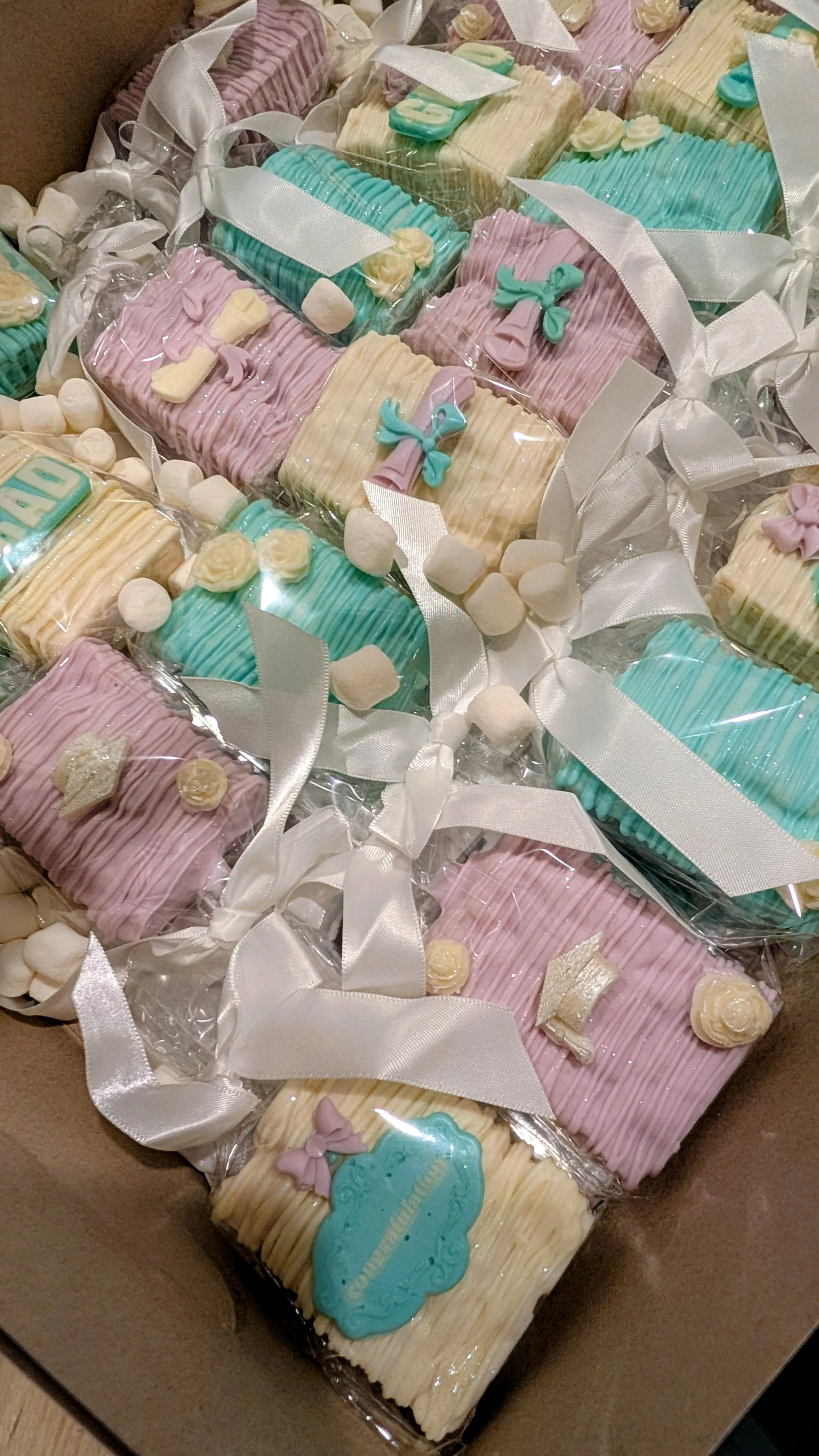 A box of pastel-colored decorated cookies wrapped in clear plastic with white ribbons, with marshmallows scattered around.