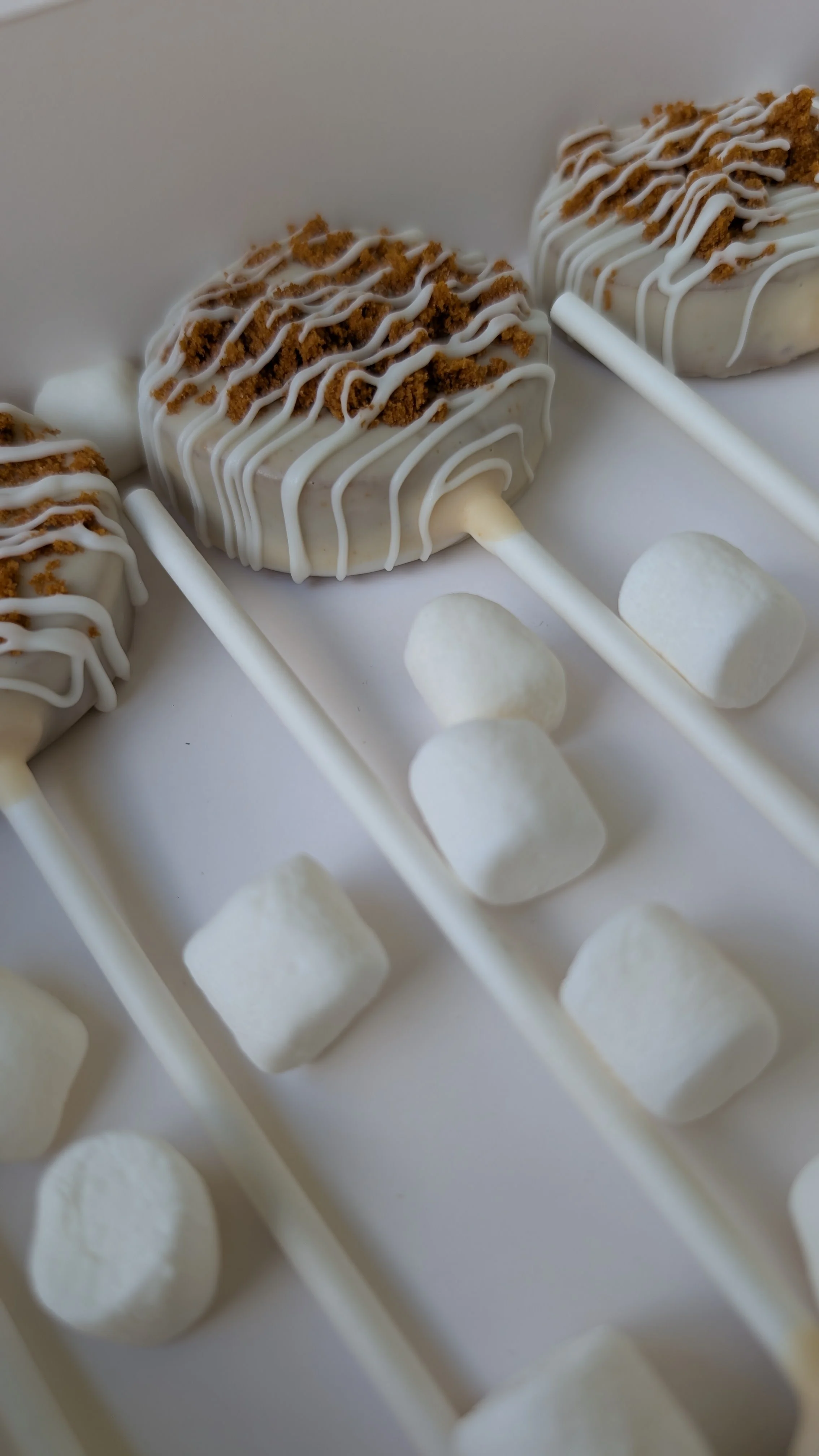Close-up of biscoff cake pops decorated with white icing and crumbled cookies, arranged in rows on a white surface.