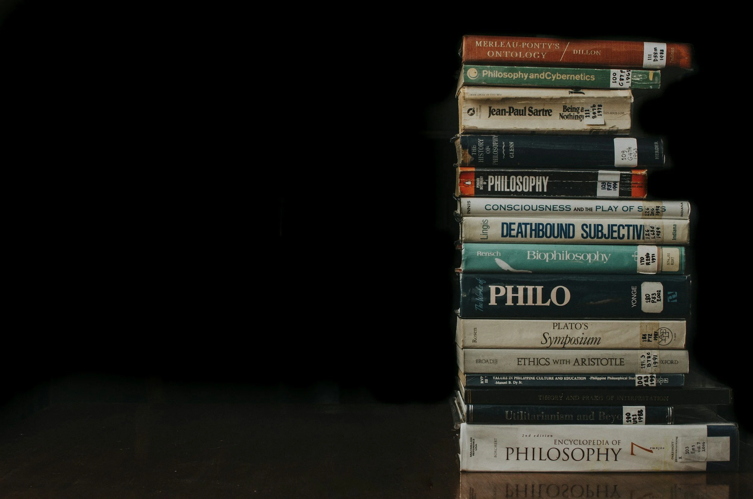 A vertical stack of various philosophical books against a black background, with some books showing wear and stickers on their spines.