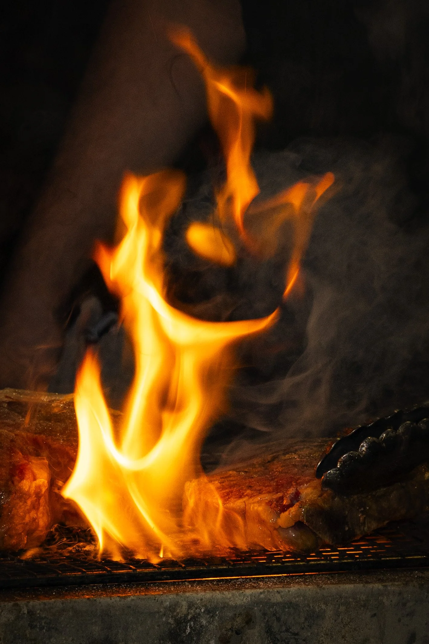 Close-up of flames and burning wood on a grill, with dark surroundings.