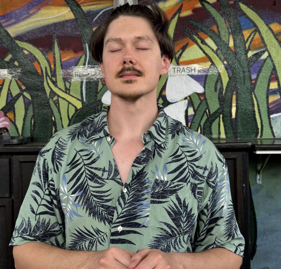 A young man with closed eyes, in a meditative state, wearing a green patterned shirt with black leaf designs