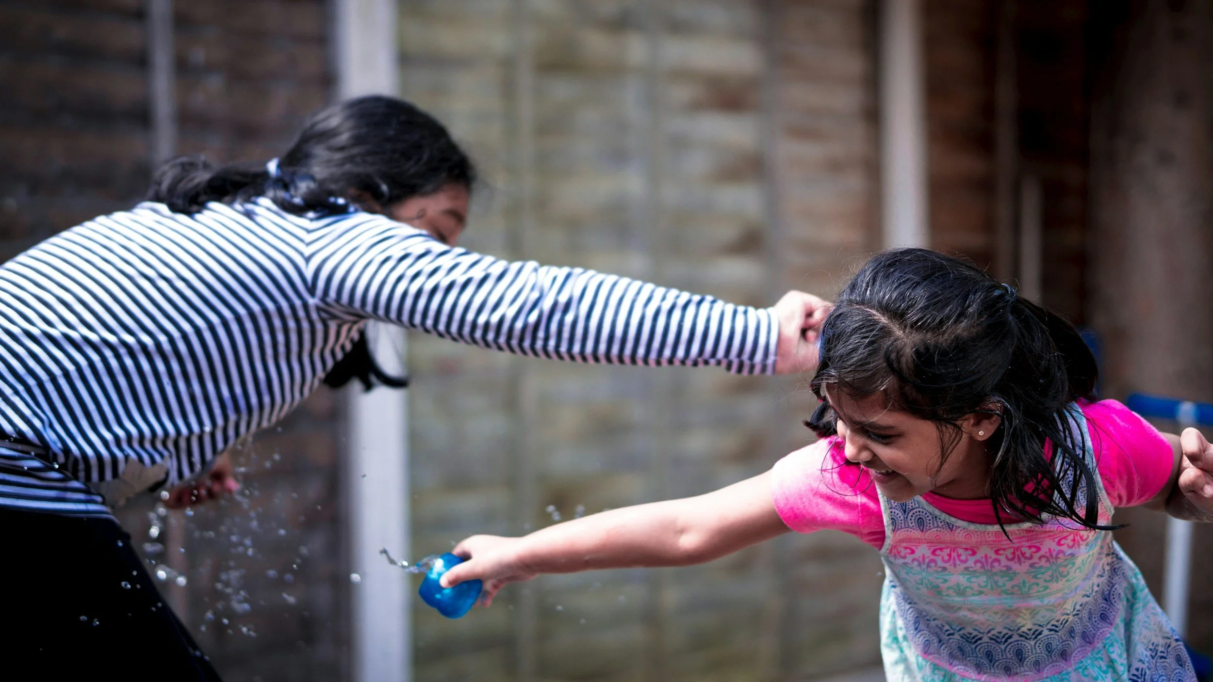Two women and a young girl playing and splashing water outdoors.