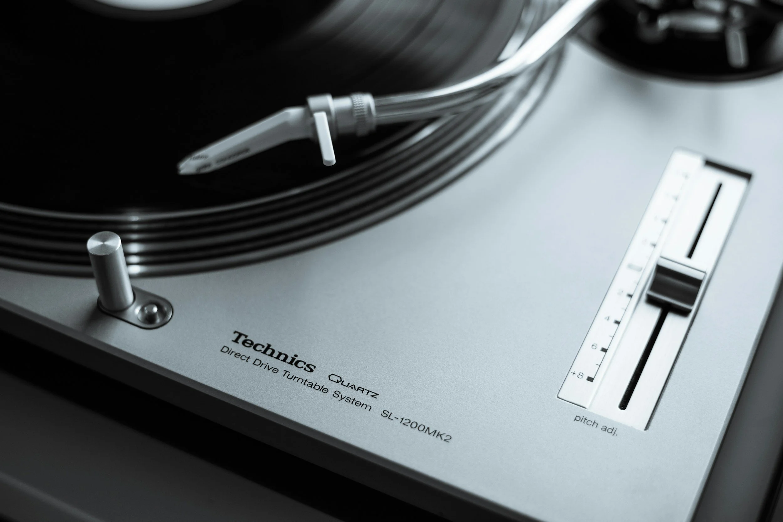 Close-up of a Technics turntable with a silver body, featuring a tonearm, pitch control slider, and brand label.