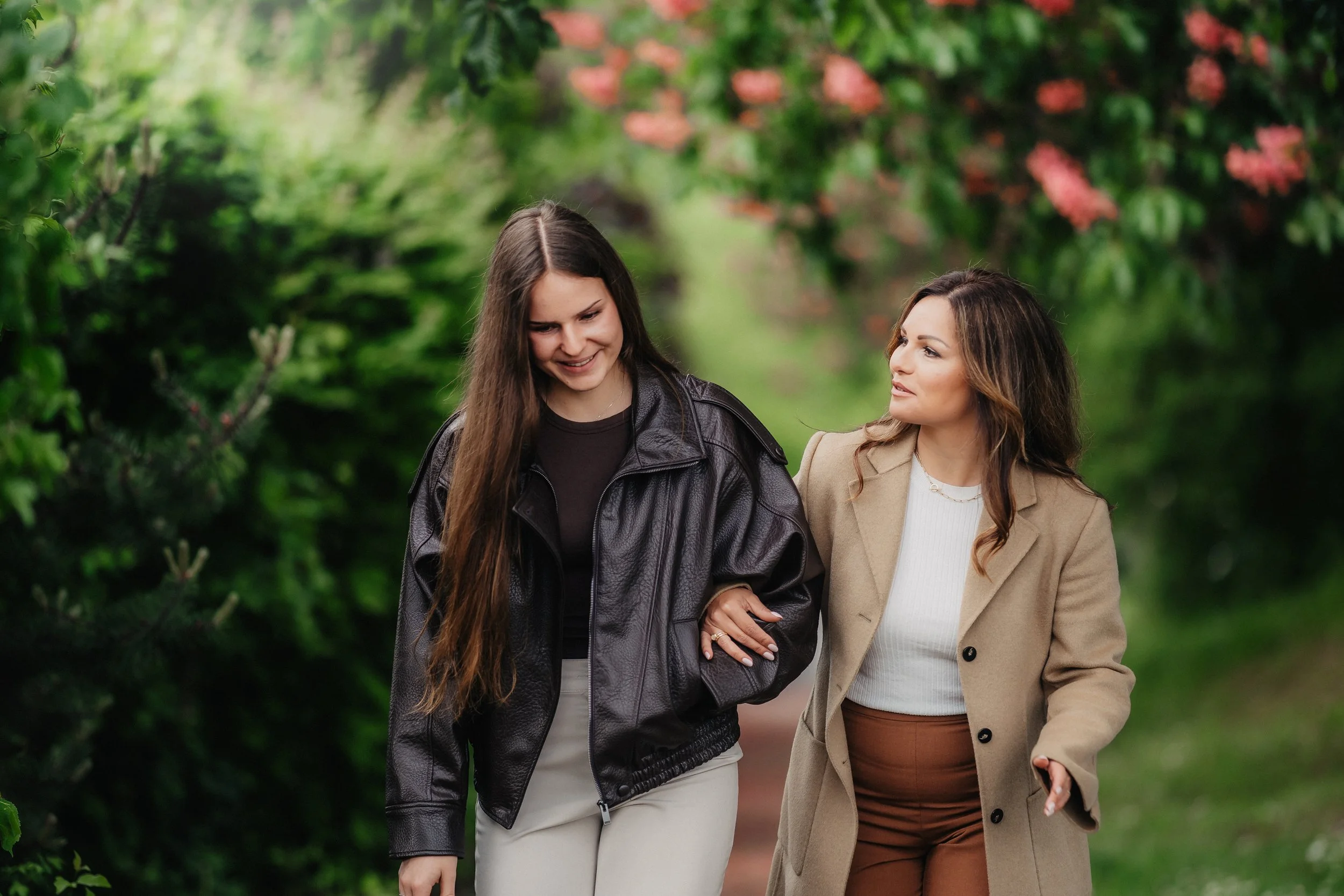 Zwei Frauen, die im Park an einer grünen, blühenden Umgebung spazieren gehen.
